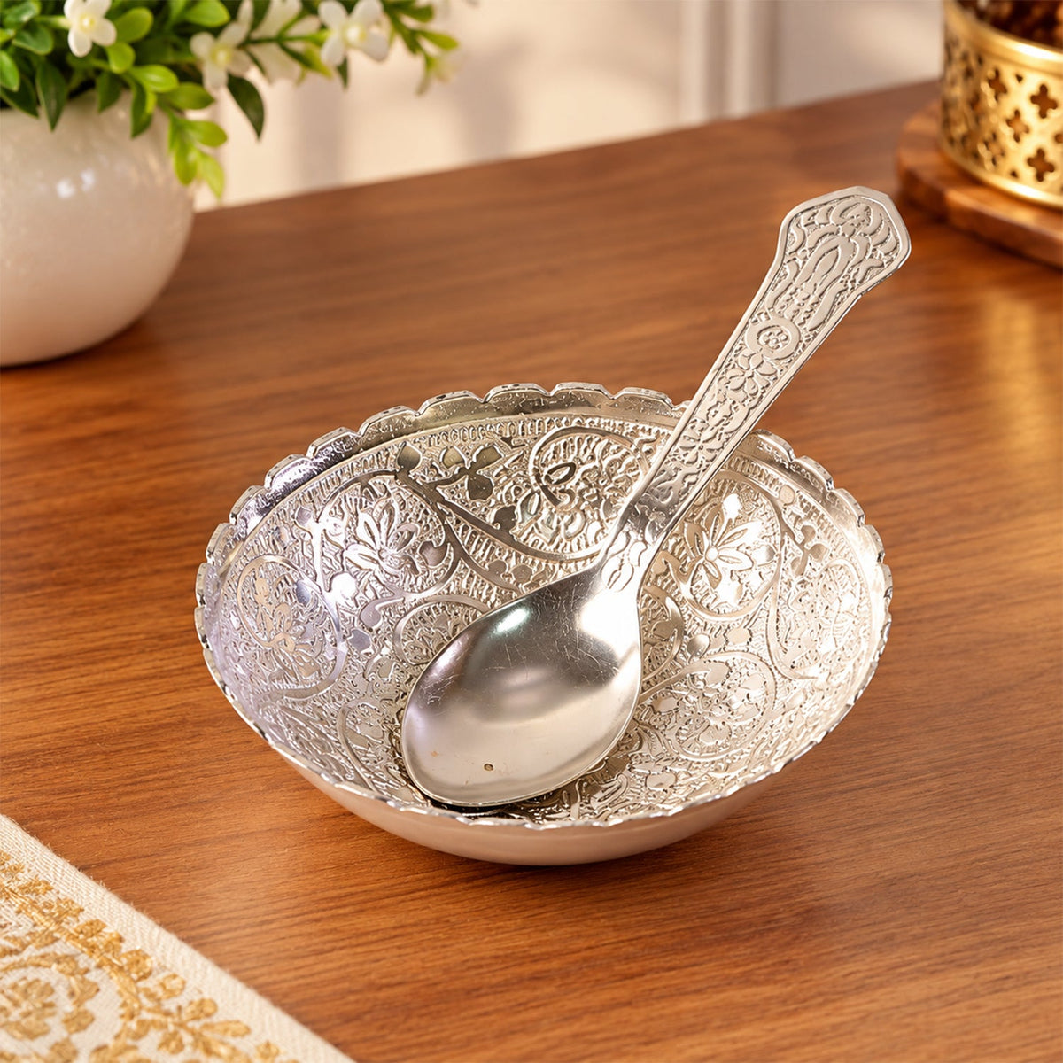 Silver finish floral serving bowl with a matching spoon resting inside, on a wooden table.