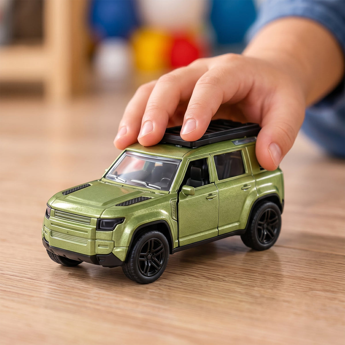 A child's hand gently pushes a metallic green die-cast SUV toy with a roof rack on a wooden floor.