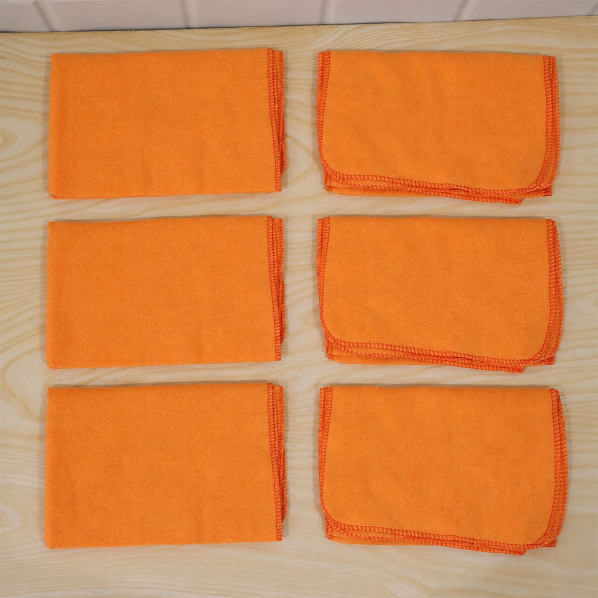 Six orange microfiber cloths, some folded, some flat, neatly arranged on a light wooden surface.