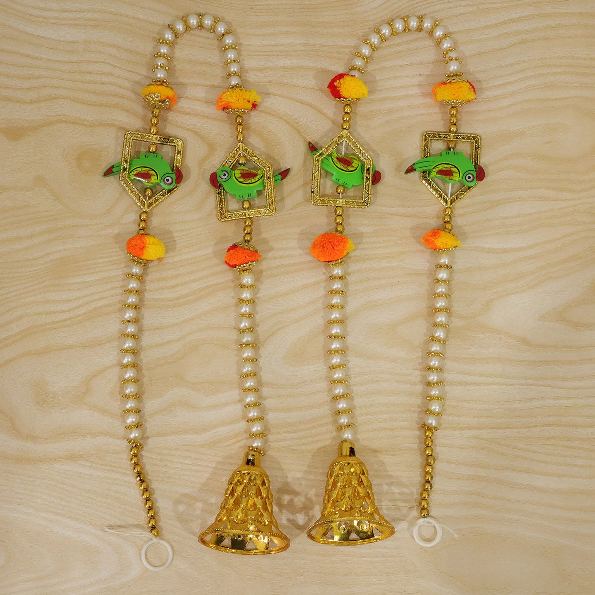 Four decorative door hangings with green parrots, orange pom-poms, and golden bells arranged on a light wooden surface.