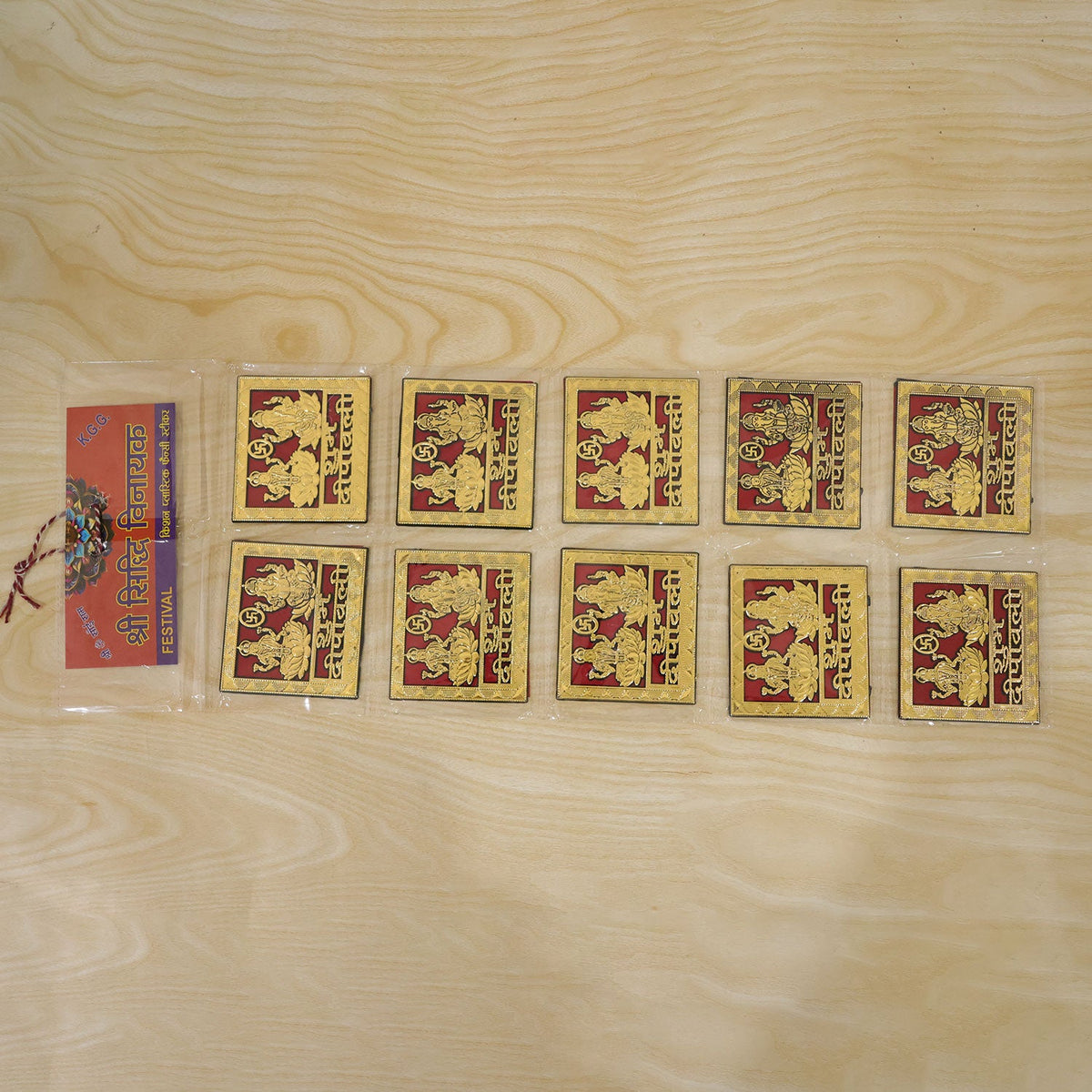 Ten square golden stickers with red backgrounds are displayed on a light wooden surface next to a small clear package.