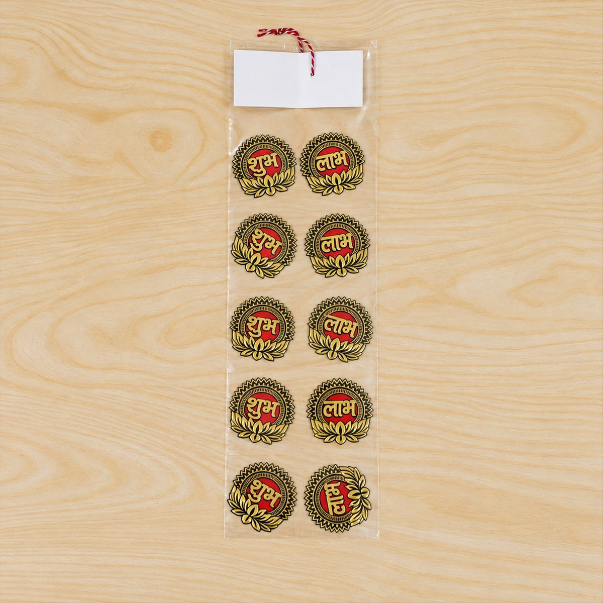 Ten gold and red Shubh Labh stickers packaged in a clear plastic sleeve with a red and white string on a wooden table.