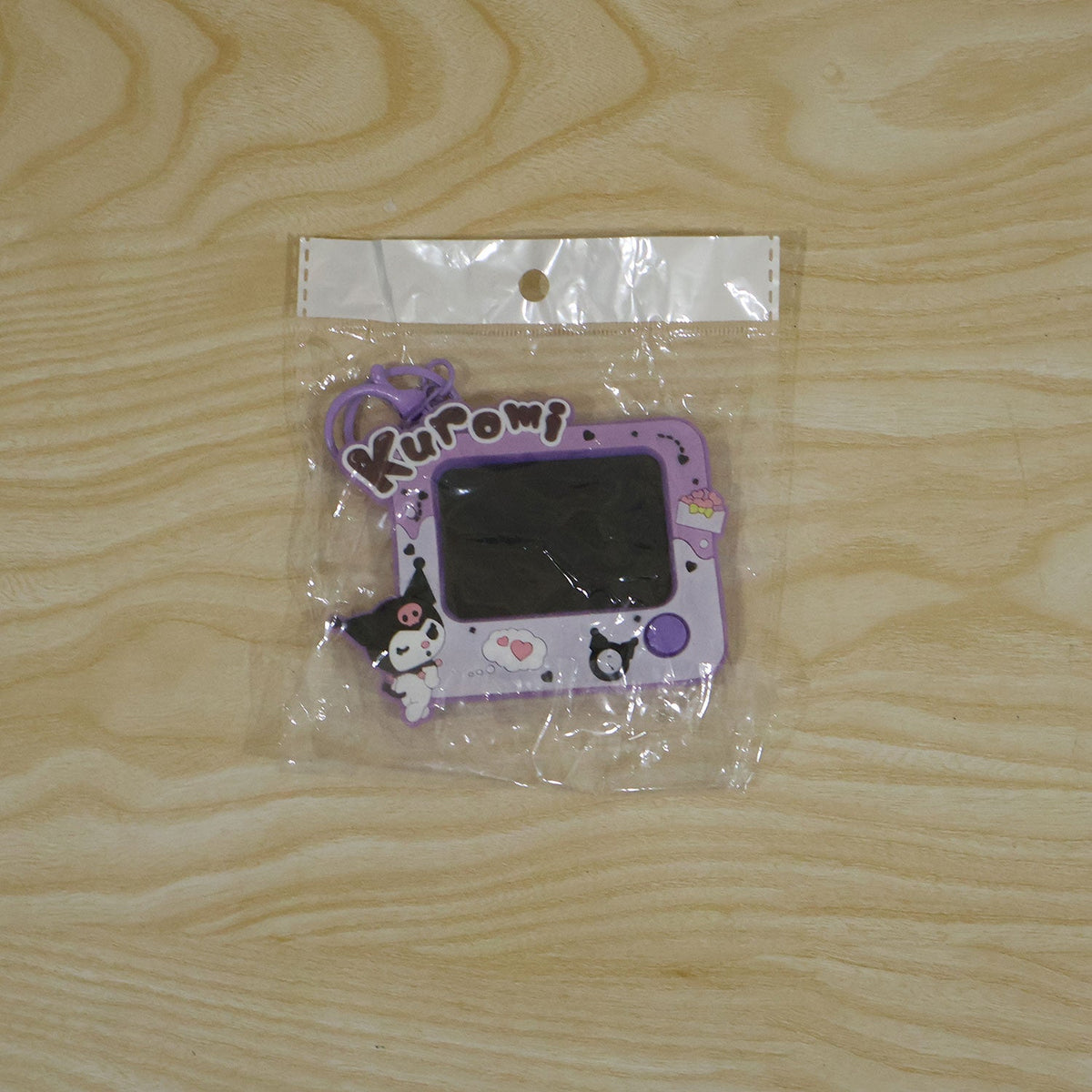 A purple Kuromi LCD writing tablet keychain, still in its clear plastic packaging, rests on a light wooden surface.