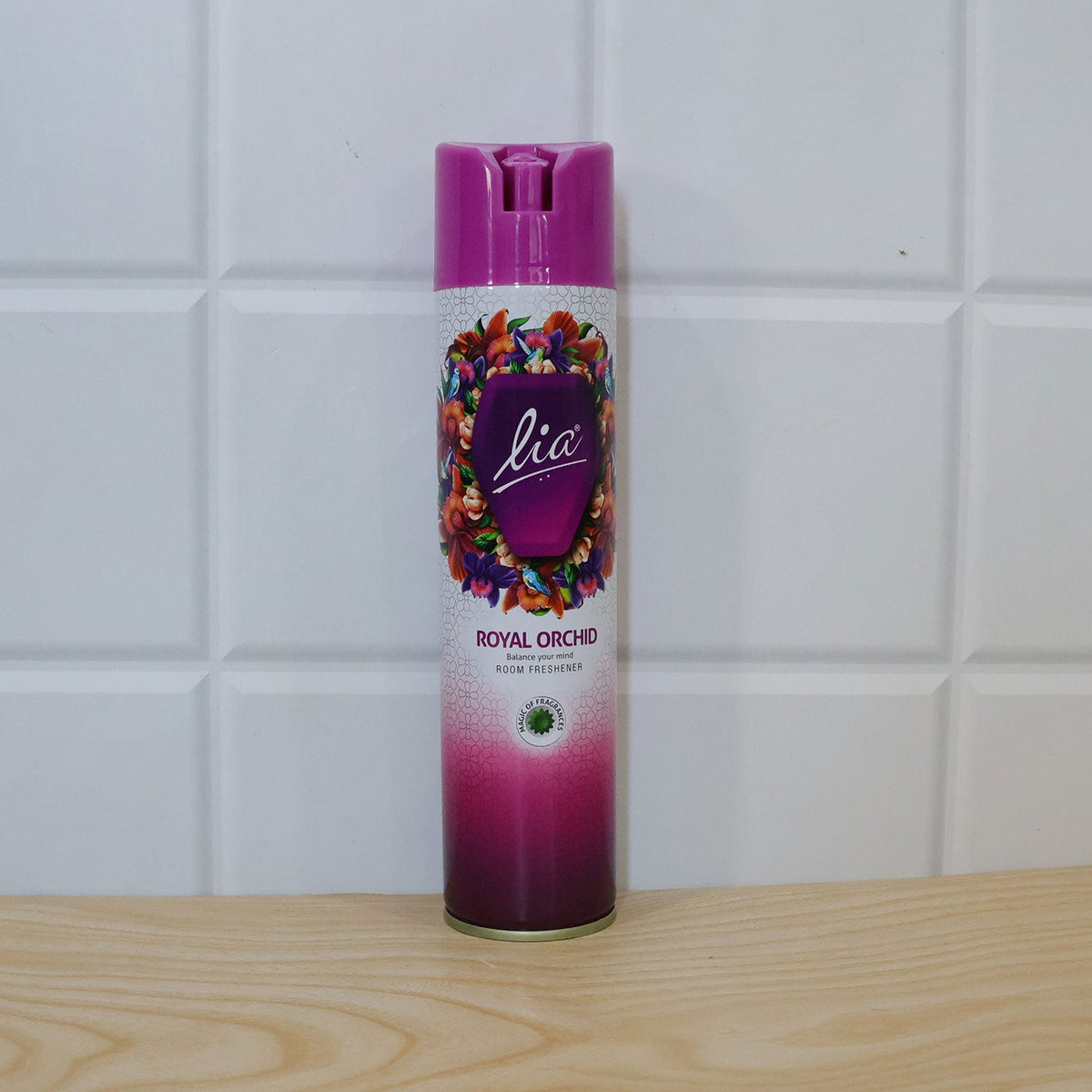 The purple and pink aerosol can stands on a light wooden surface against a white tiled wall.