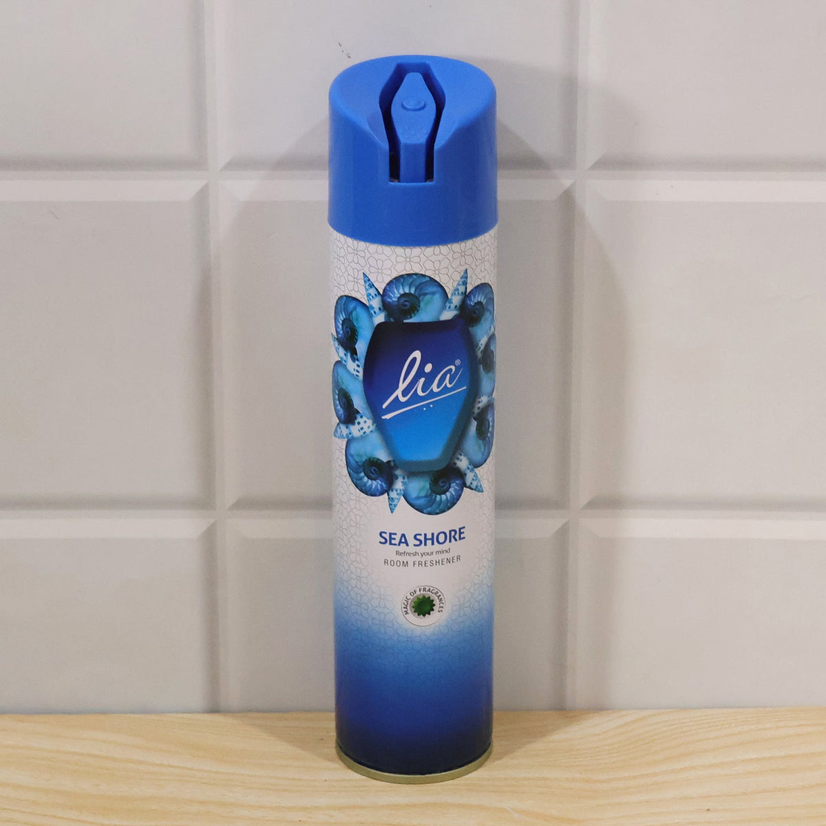 A blue and white aerosol spray can with a seashell design stands on a wooden surface against white tiles.
