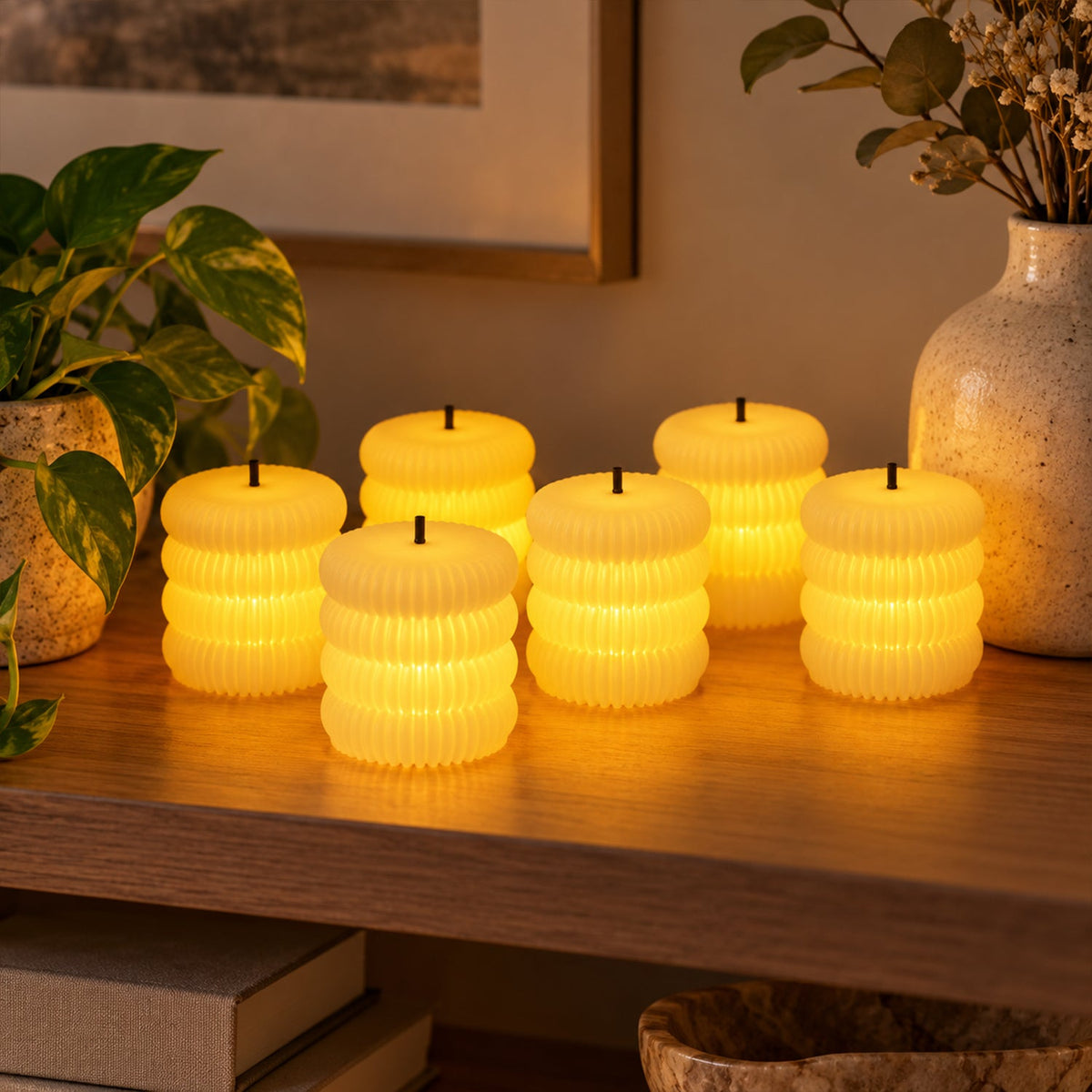 Six glowing ribbed flameless LED tealight candles on a wooden shelf next to potted plants and a vase.