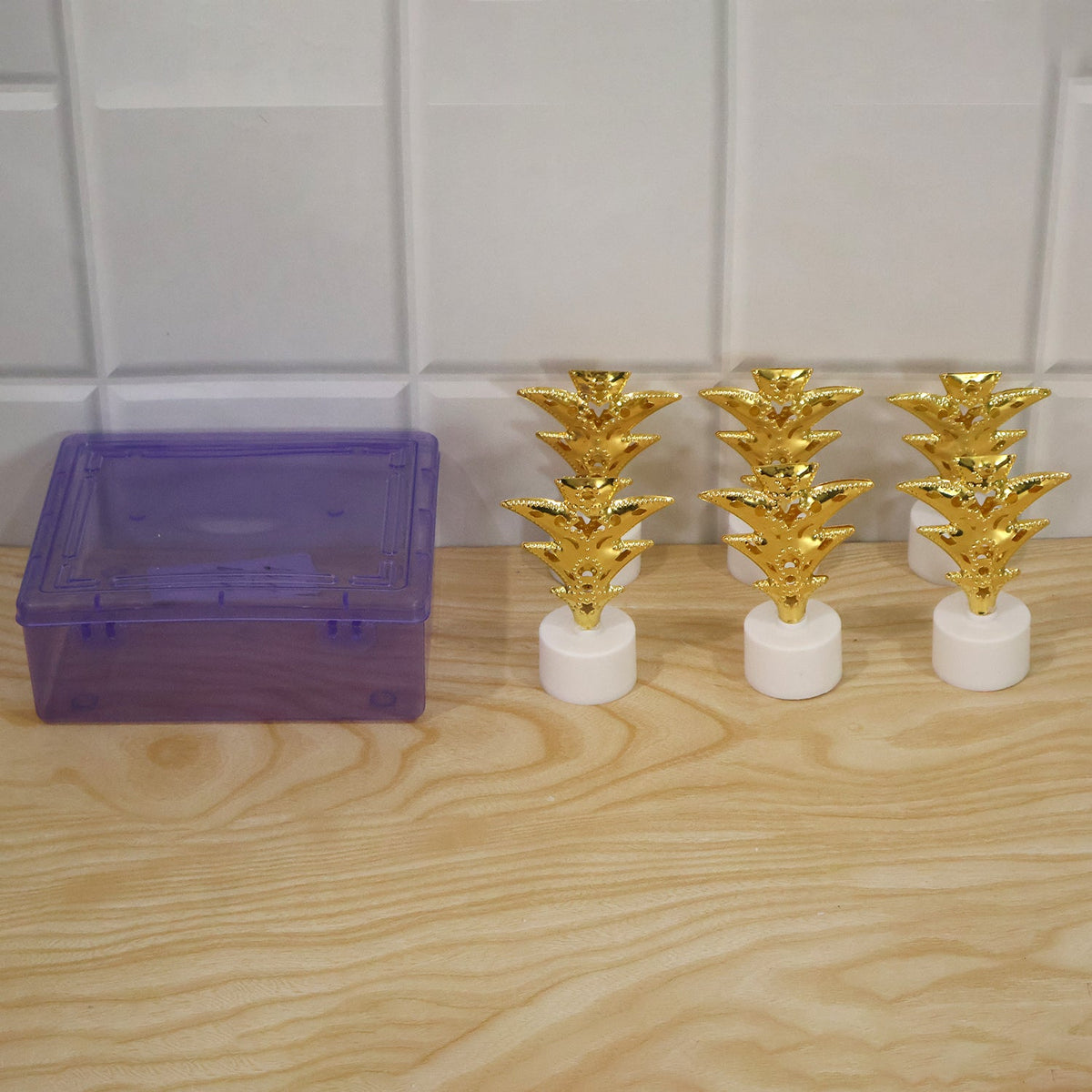 Six golden pineapple LED tealights next to a translucent purple storage box on a wooden surface.