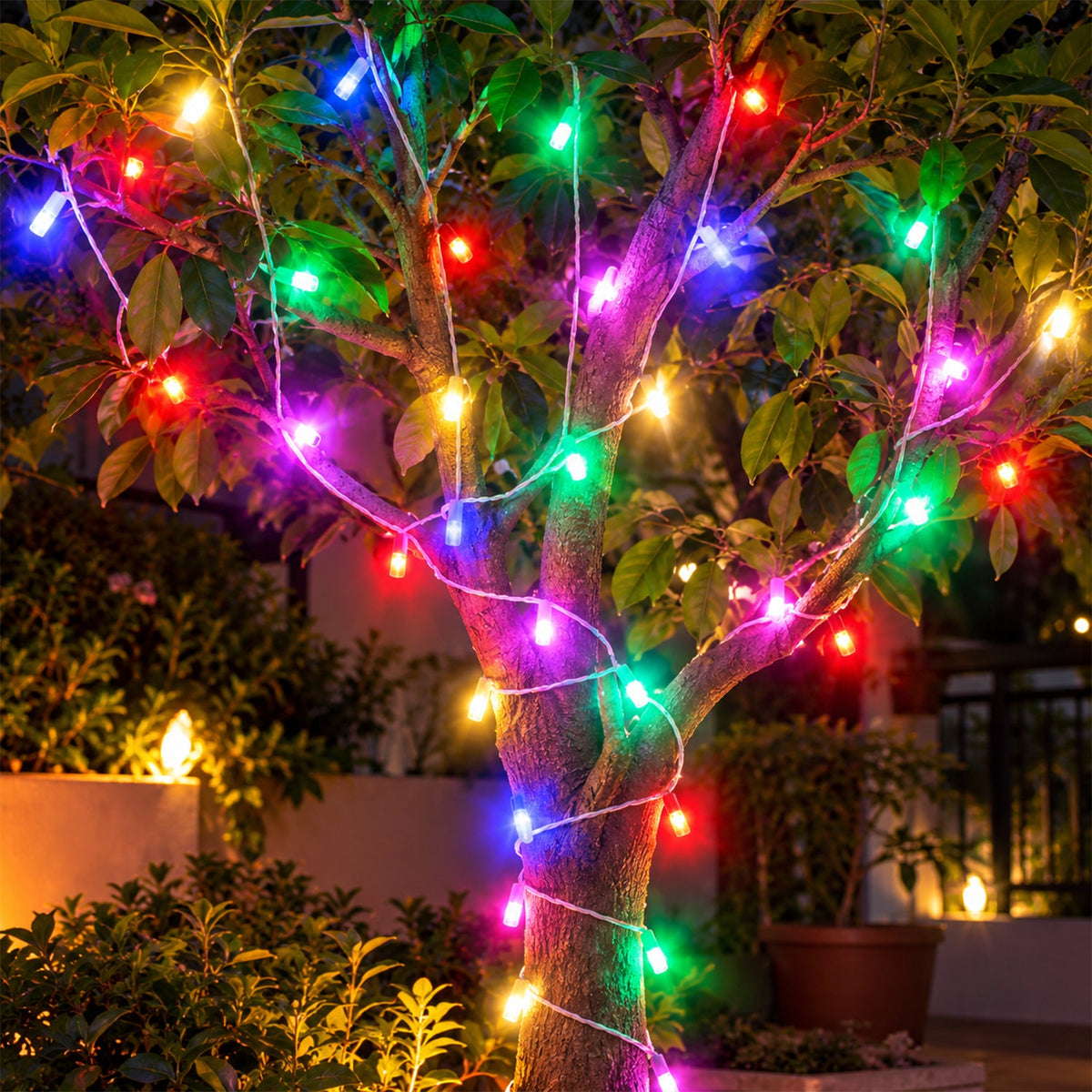 Vibrant multi-color LED string lights wrapped around a small tree in a garden at night.