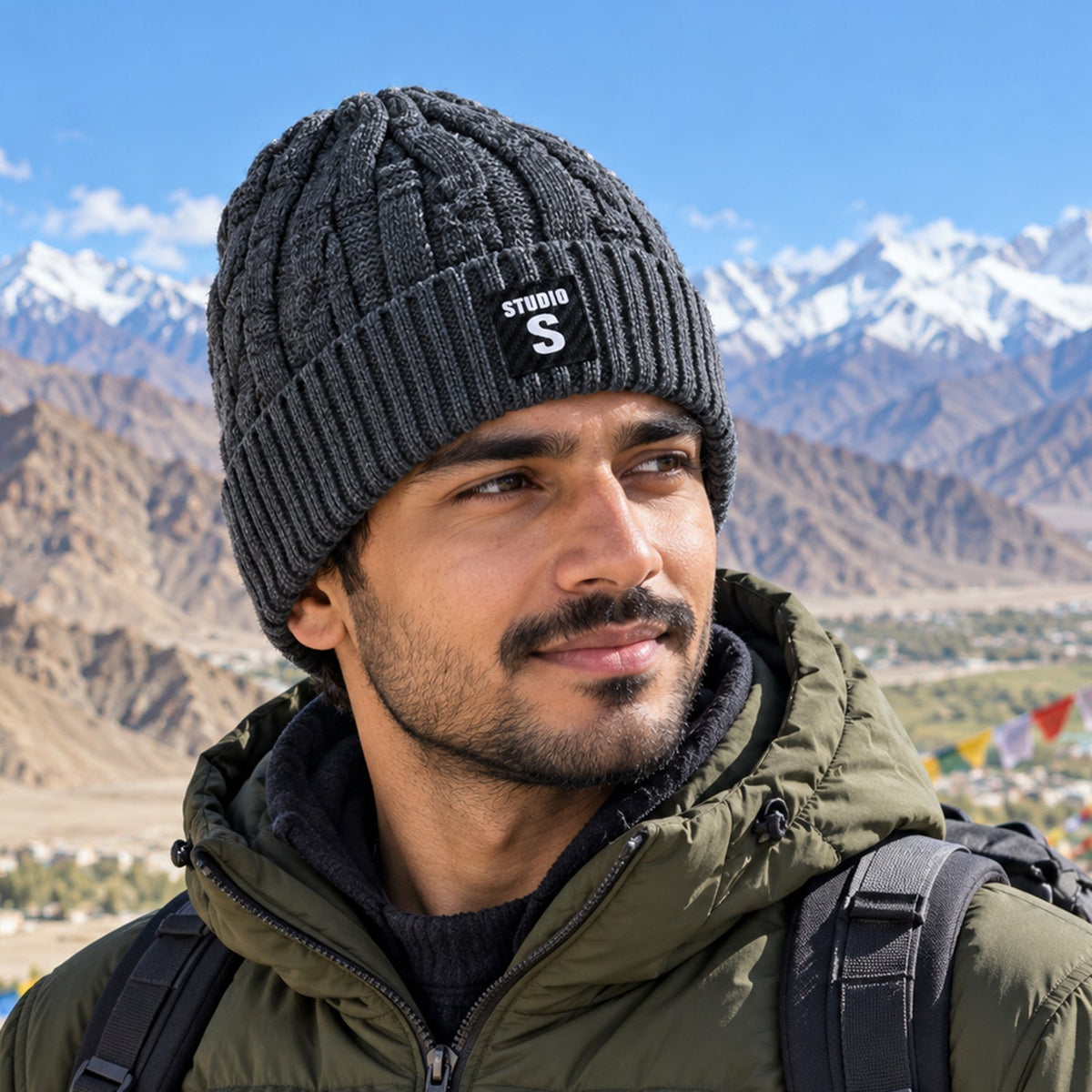 A man wearing a dark grey cable knit beanie with a folded ribbed cuff and a black label with "STUDIO S" in white, against a