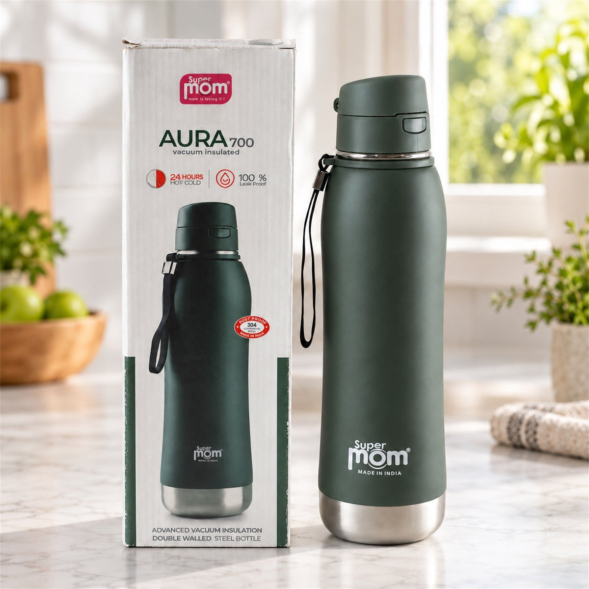 A dark green insulated stainless steel water bottle stands next to its product packaging on a kitchen counter with plants.