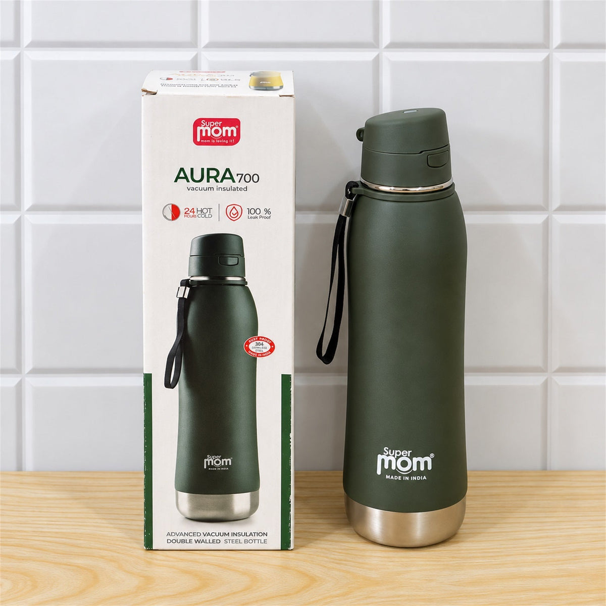 A dark green insulated stainless steel water bottle stands next to its product packaging on a wooden surface against white