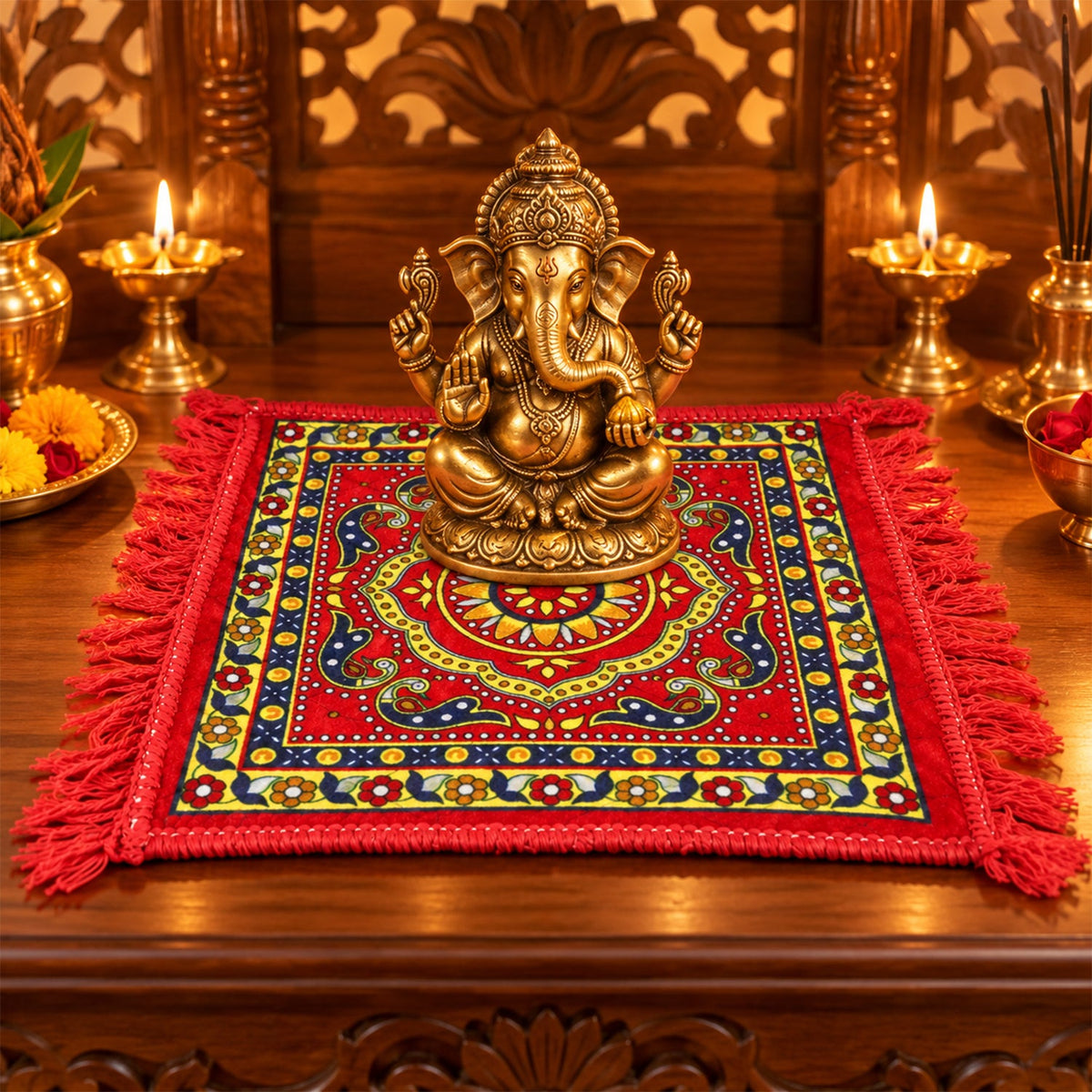 A red prayer mat with a yellow and blue traditional pattern and fringe, with a golden Ganesha idol on top.