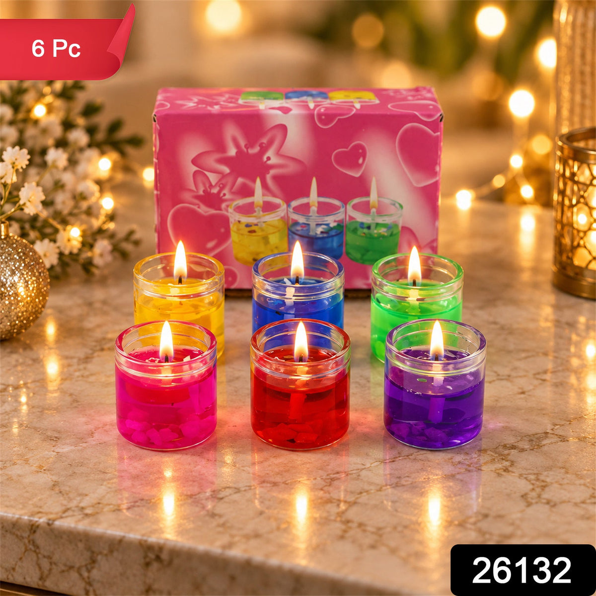 Six lit gel candles in glass jars, in yellow, blue, green, pink, red, and purple, arranged around a pink box. – view 2