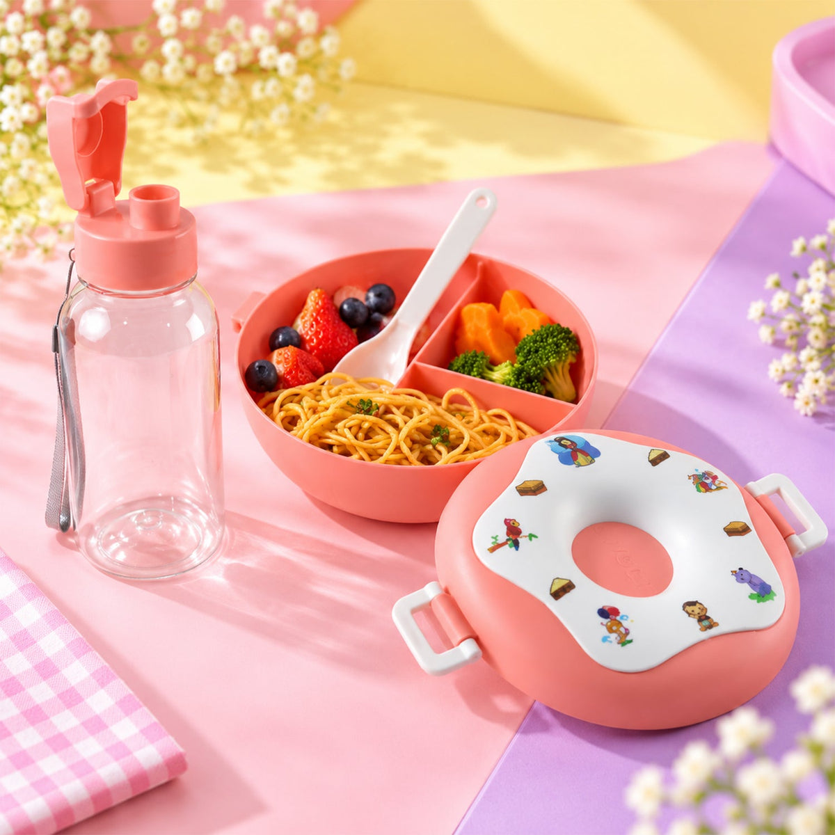 A pink donut-shaped lunch box, a clear water bottle, and a divided bowl filled with pasta, fruit, and vegetables on a