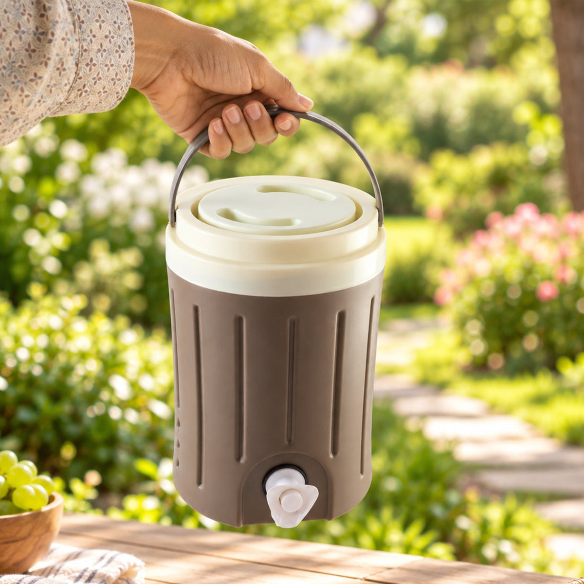 A hand holds the brown and cream insulated jug by its handle outdoors with green foliage in the background.