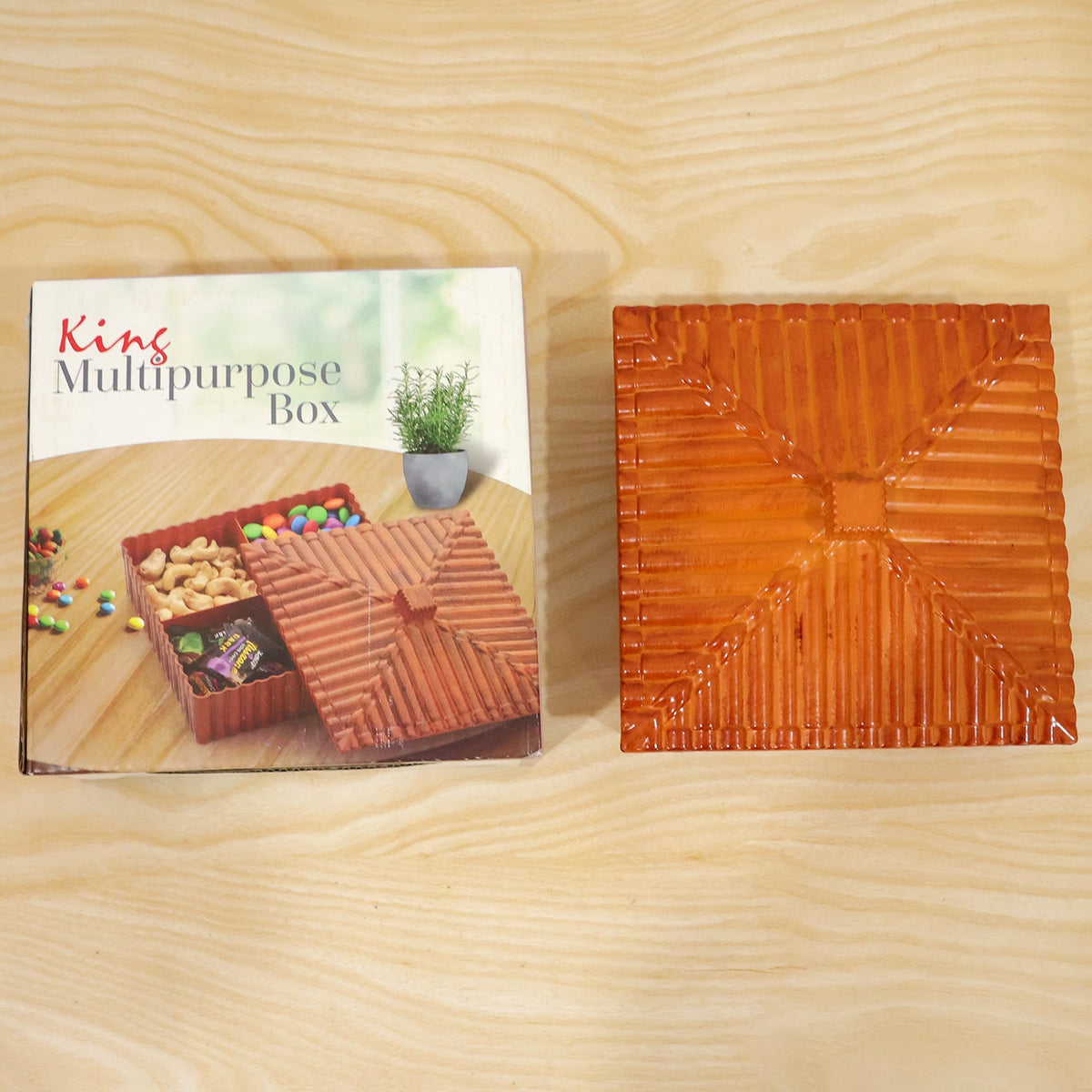 A brown square dry fruit box with a ribbed lid is shown next to its product packaging on a light wooden surface.
