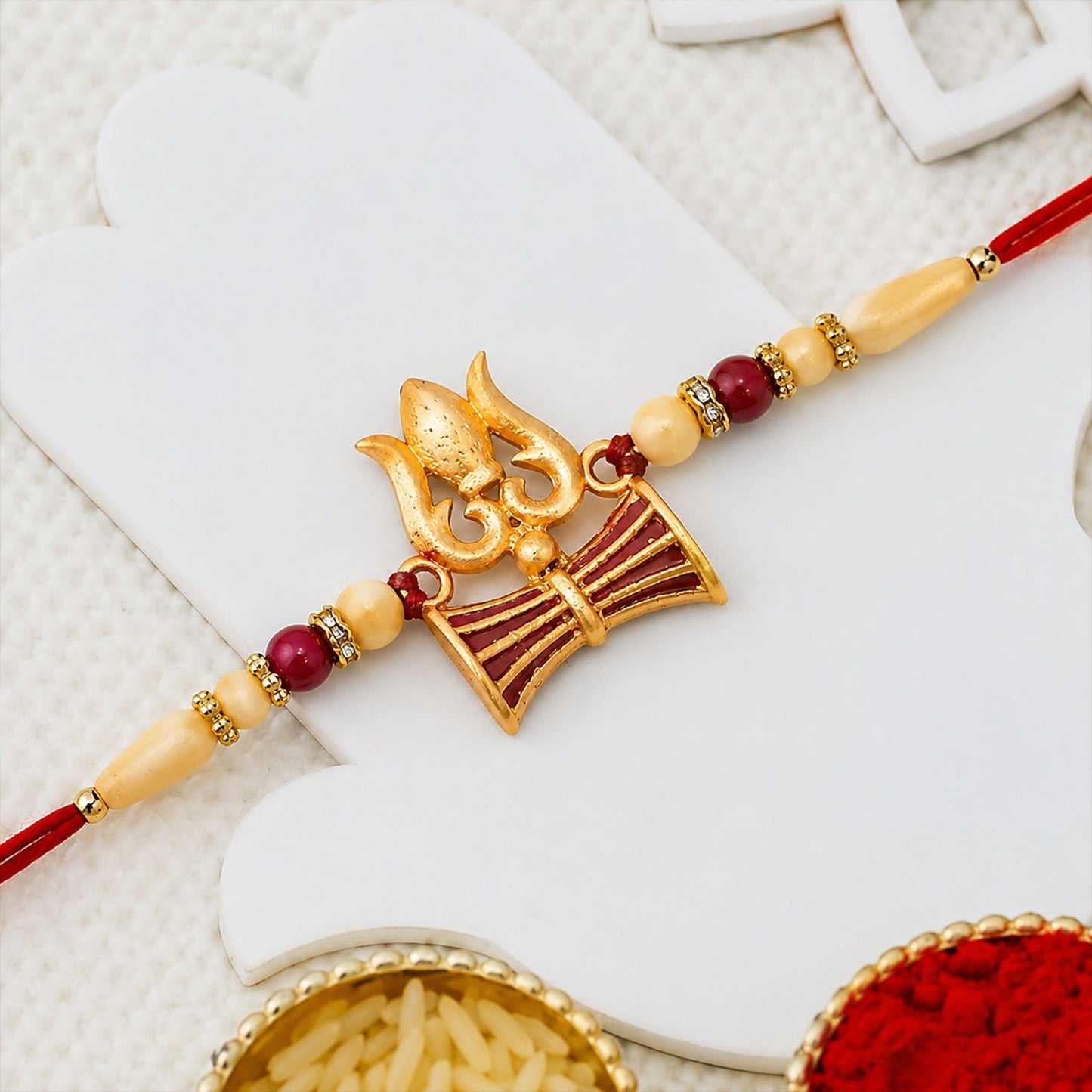 Close-up of Shiva Trishul Rakhi with red and golden bead embellishments symbolizing protection.