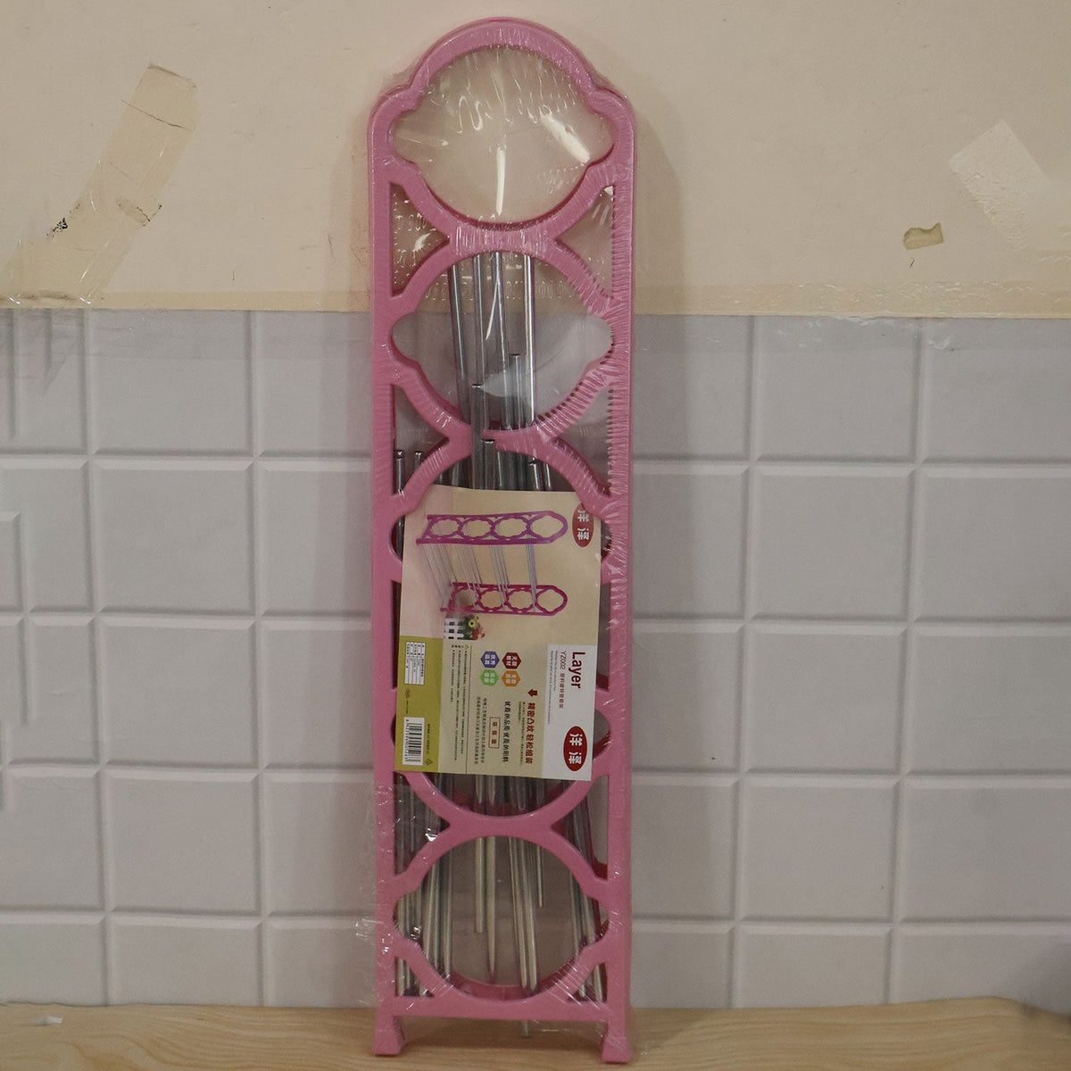 A pink shoe rack disassembled and packaged in clear plastic, leaning against a tiled wall.
