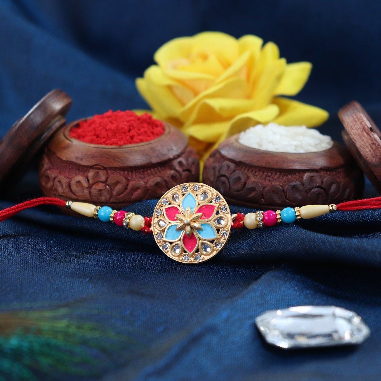 Round floral rakhi featuring pink and blue enamel with beaded thread detail