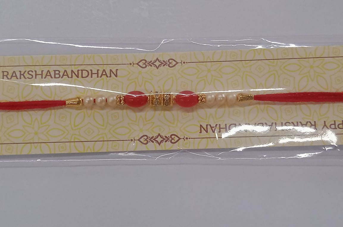 Traditional Pearl Beaded Rakhi with red and gold decorative elements placed on woven fabric.