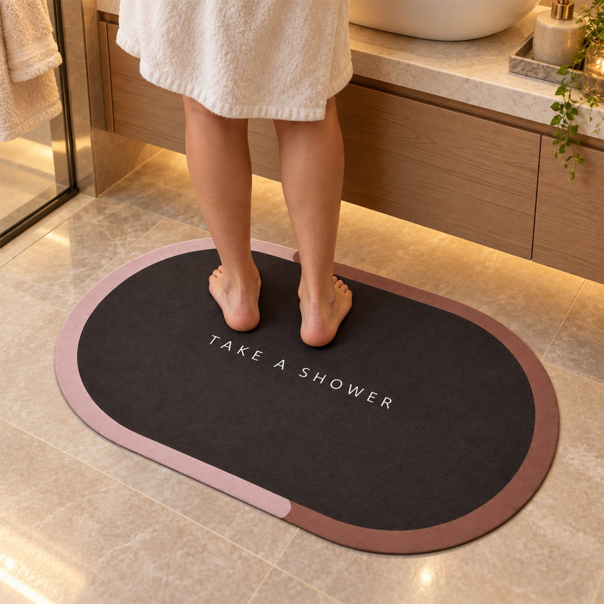 A person stands barefoot on a dark oval bath mat with a pink and brown edge, in a modern bathroom setting.