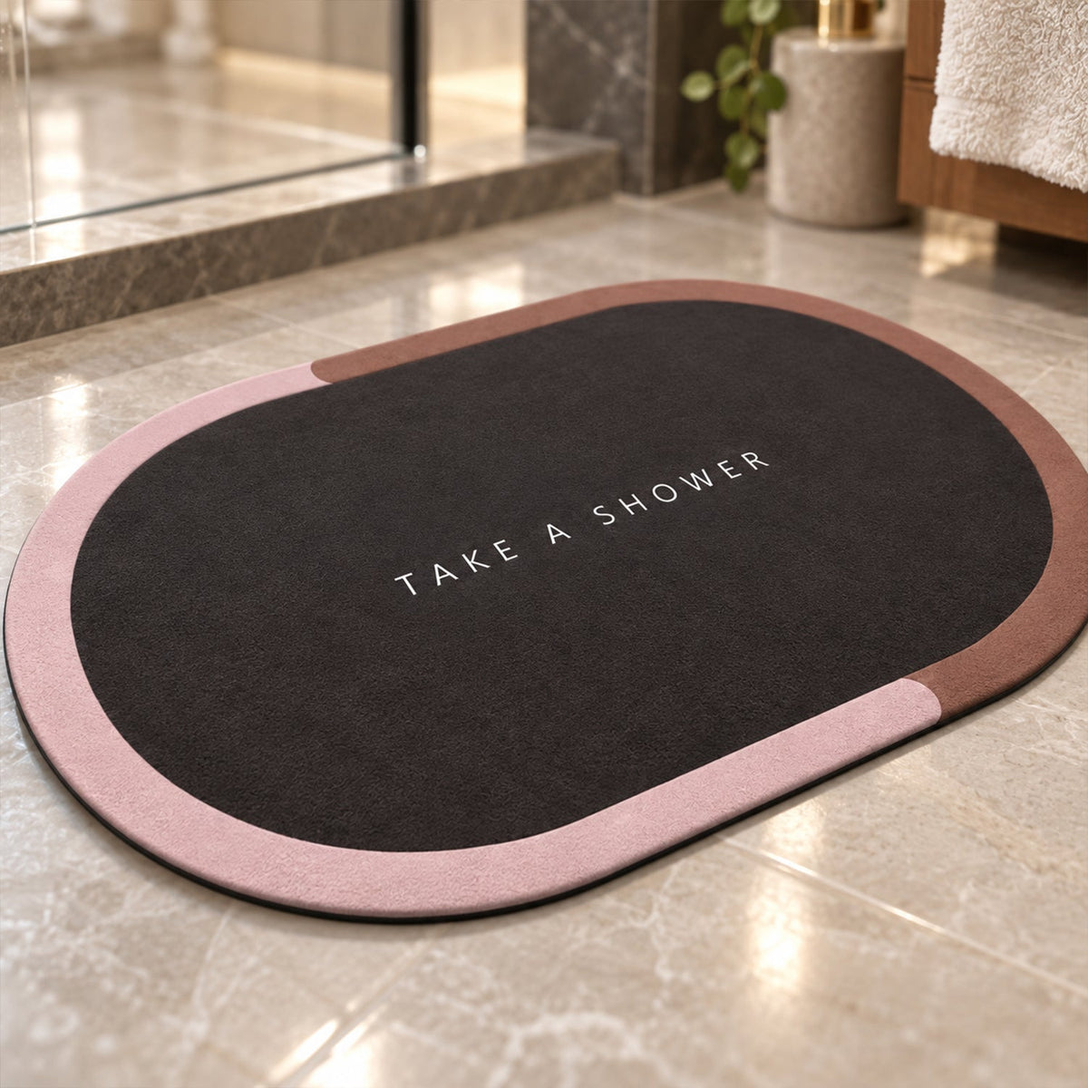 A dark oval bath mat with a pink and brown border rests on a light marble floor in a luxurious bathroom.