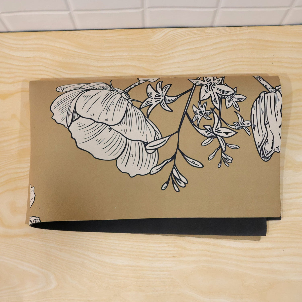 The mustard yellow mat with white floral designs is folded neatly on a light wooden surface.