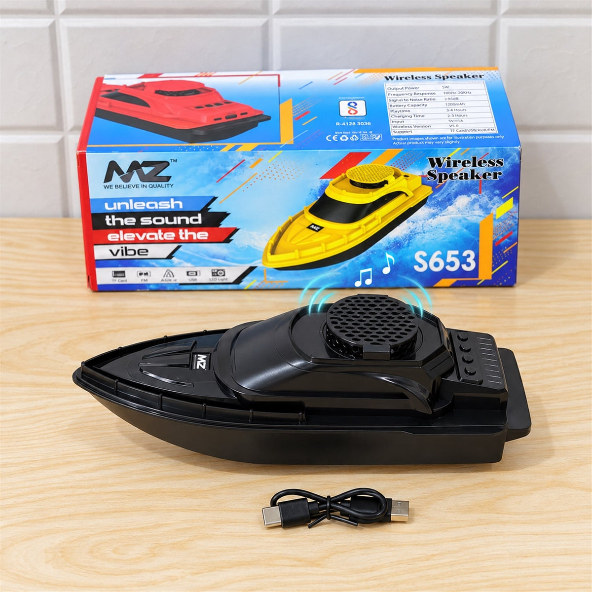 A black boat-shaped speaker sits on a wooden surface, with its colorful retail packaging box displayed behind it.