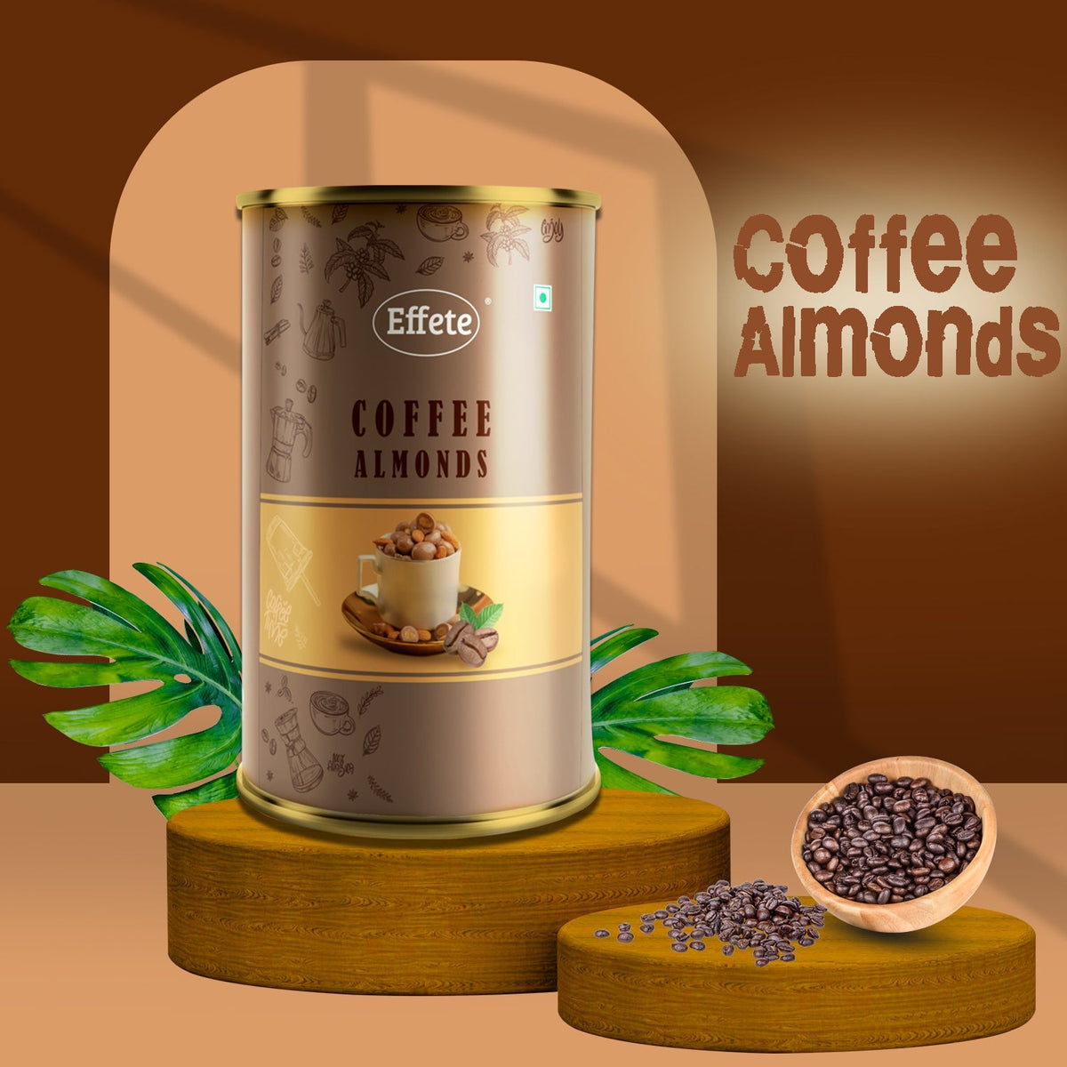Brown and gold tin of coffee almonds on a yellow pedestal with coffee beans in a bowl and scattered, and a large green leaf.