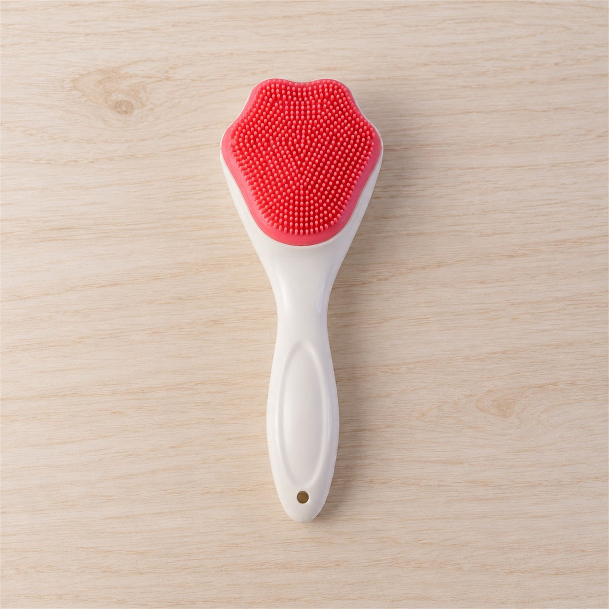 A white-handled brush with a pink, paw-shaped silicone head is positioned centrally on a light wooden surface.