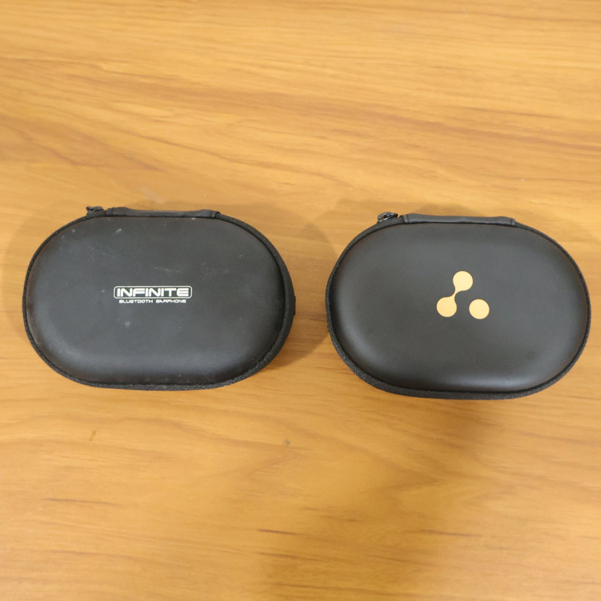 Two closed black hard shell cases are side-by-side on a wooden surface, one with a logo, the other with text.