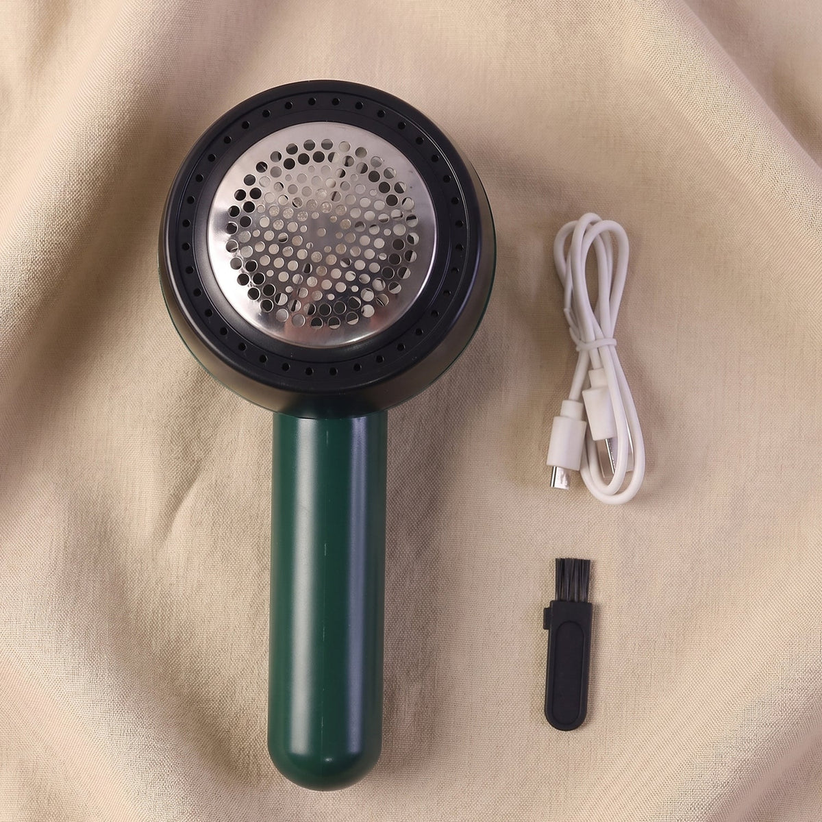 A dark green and black lint remover, white USB-C charging cable, and small black cleaning brush are displayed on a beige
