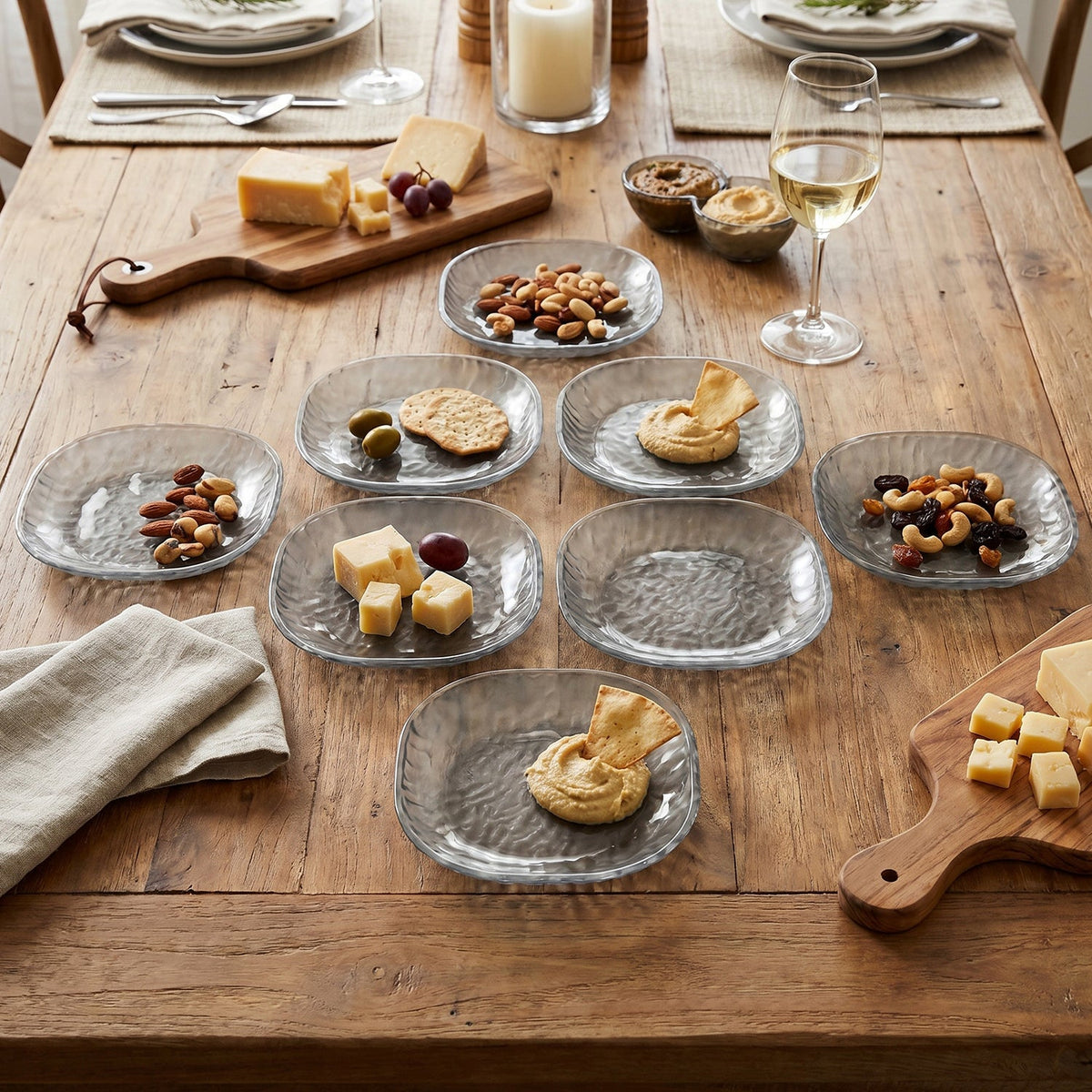 A wooden table set with eight clear textured glass snack bowls containing various appetizers, alongside wine and cheese.