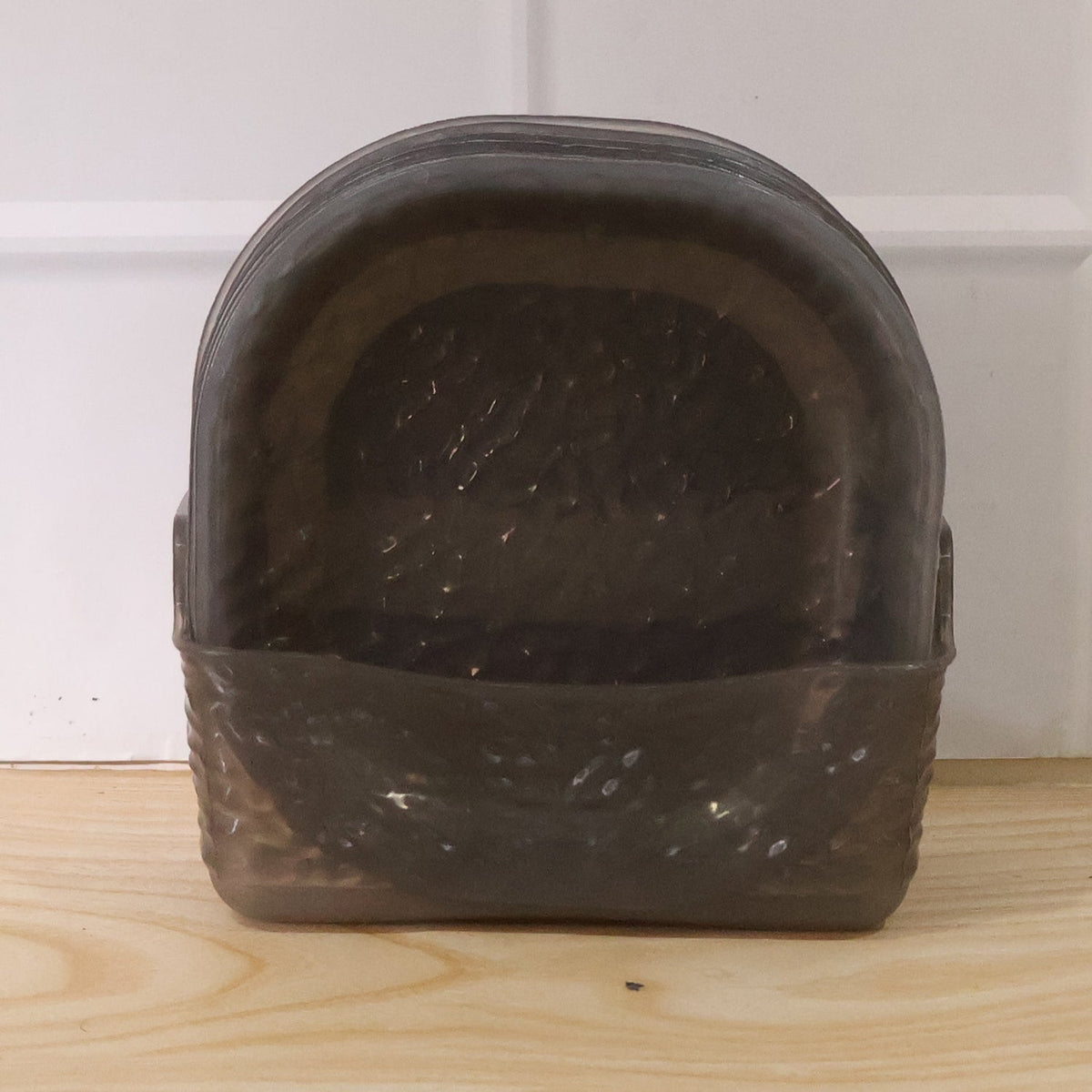 A dark gray textured glass storage basket containing multiple matching bowls, sitting on a light wooden surface.