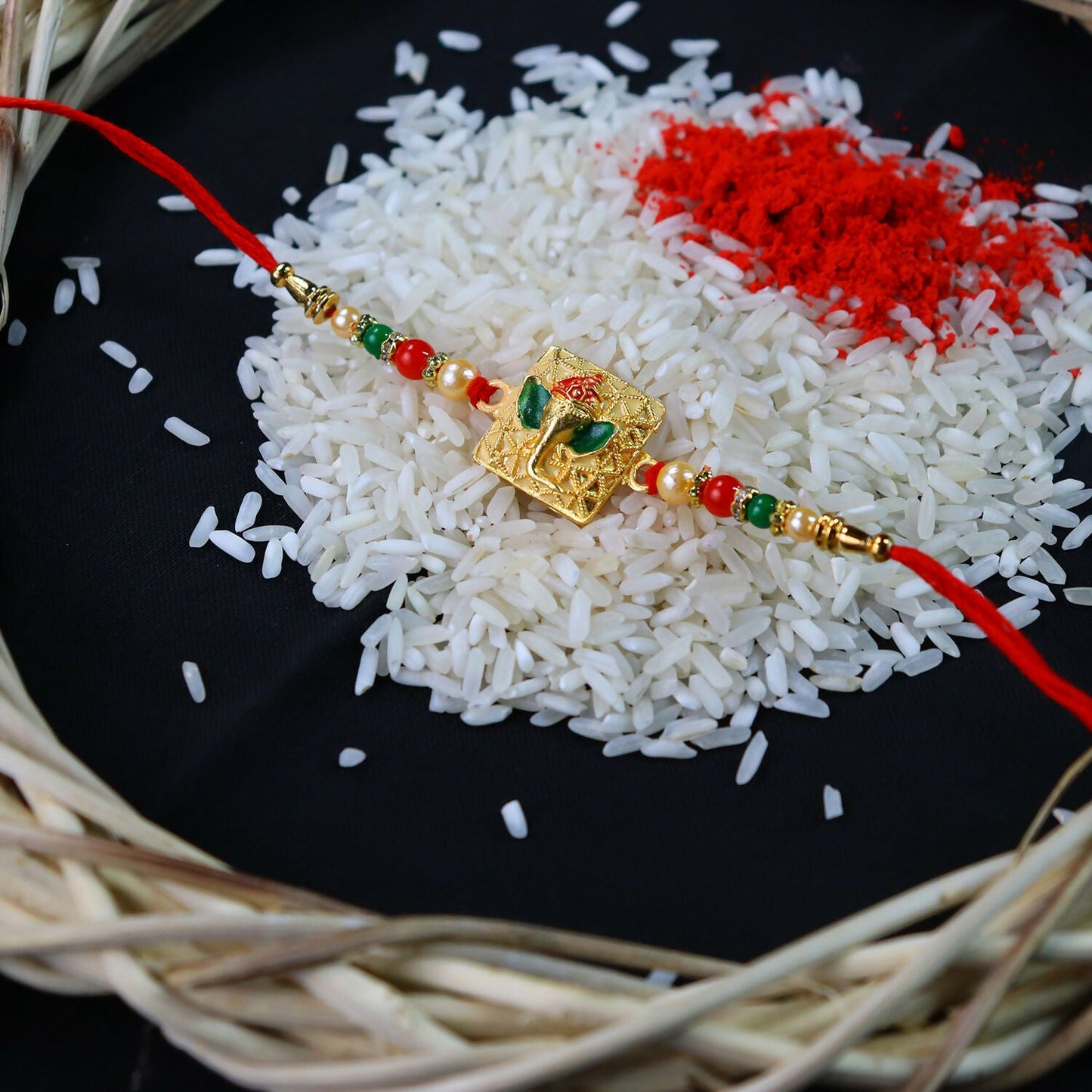Golden Ganpati Rakhi featuring red and green beads and delicate enamel detailing