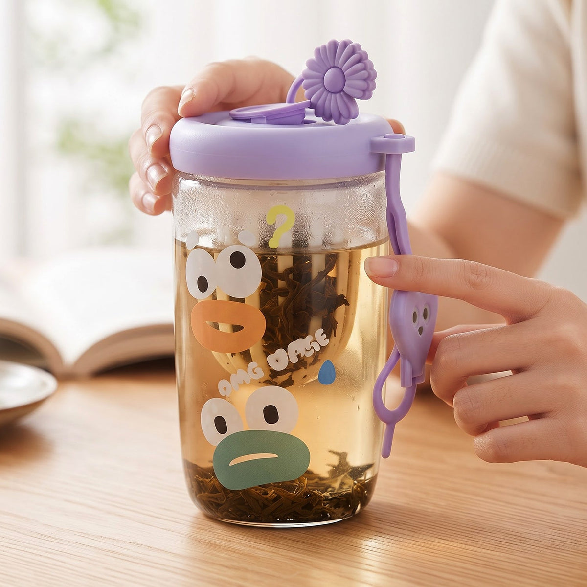 A person uses a glass tea sipper cup with a purple lid and cartoon duck face design, showing the infuser filled with loose