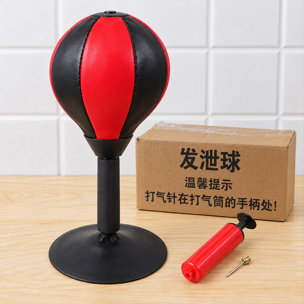 A red and black desktop punching ball with a black base, a red pump, and a cardboard box with Chinese characters.
