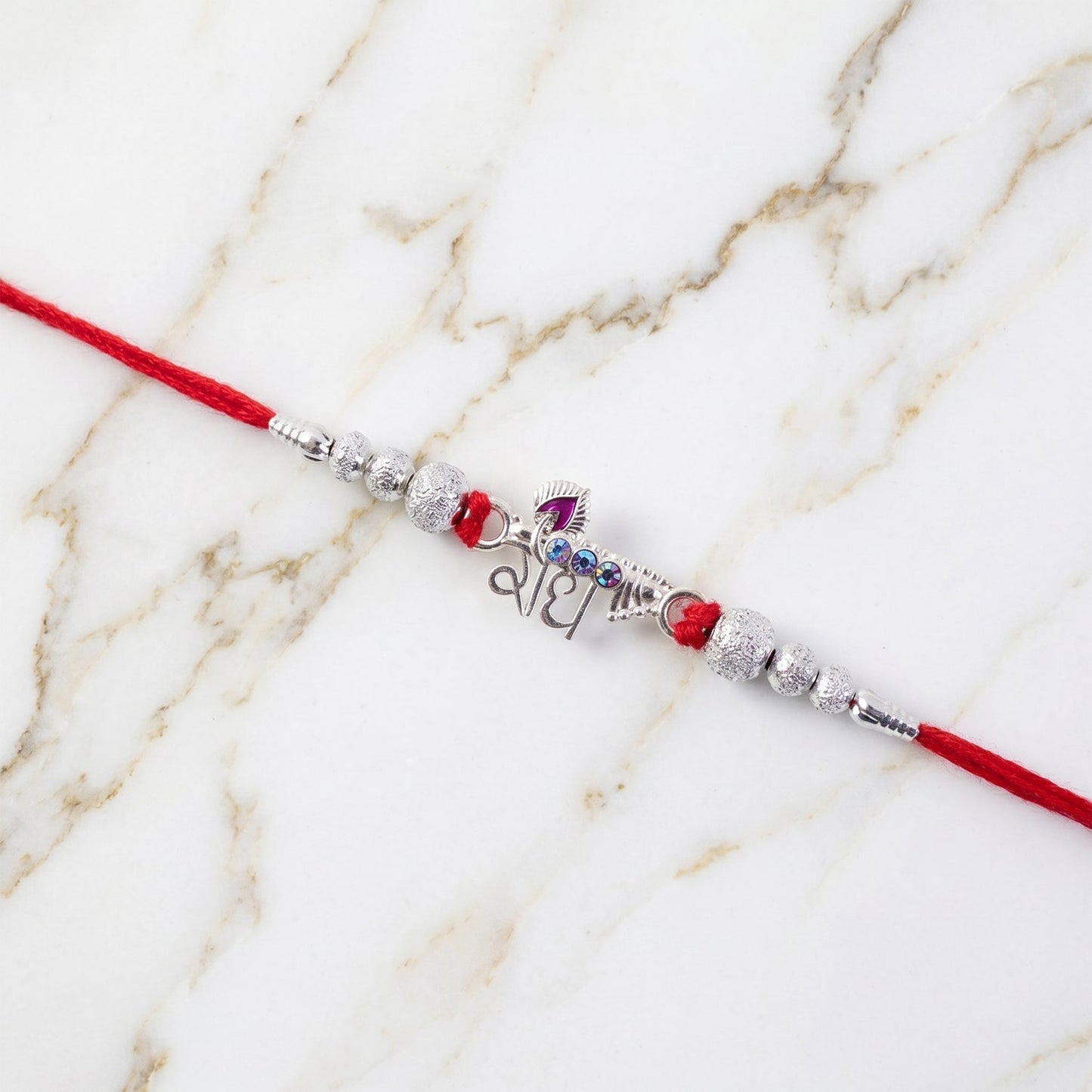 Flat lay of Radhe Silver Rakhi showing full design and red thread.
