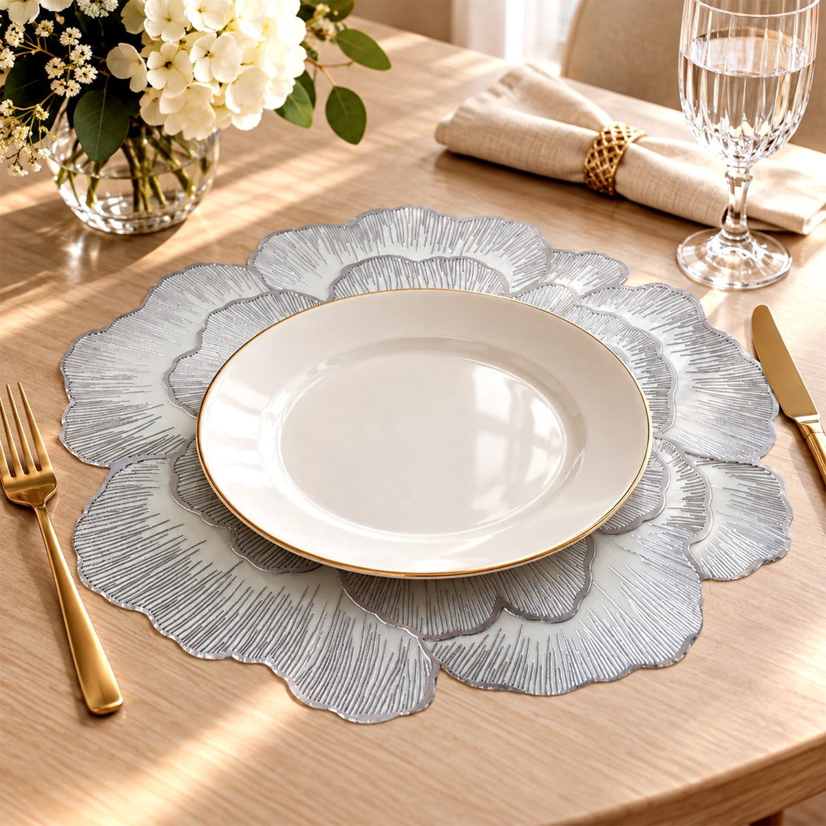 A silver floral placemat with a white plate, golden fork, and knife on a wooden table.