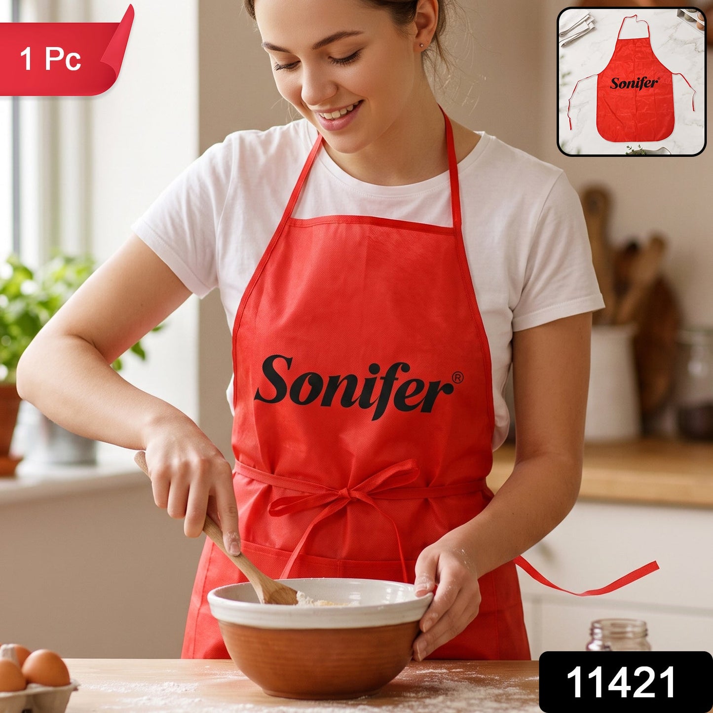 A smiling woman in a white t-shirt and a red Sonifer apron stirs batter in a bowl on a wooden counter, with