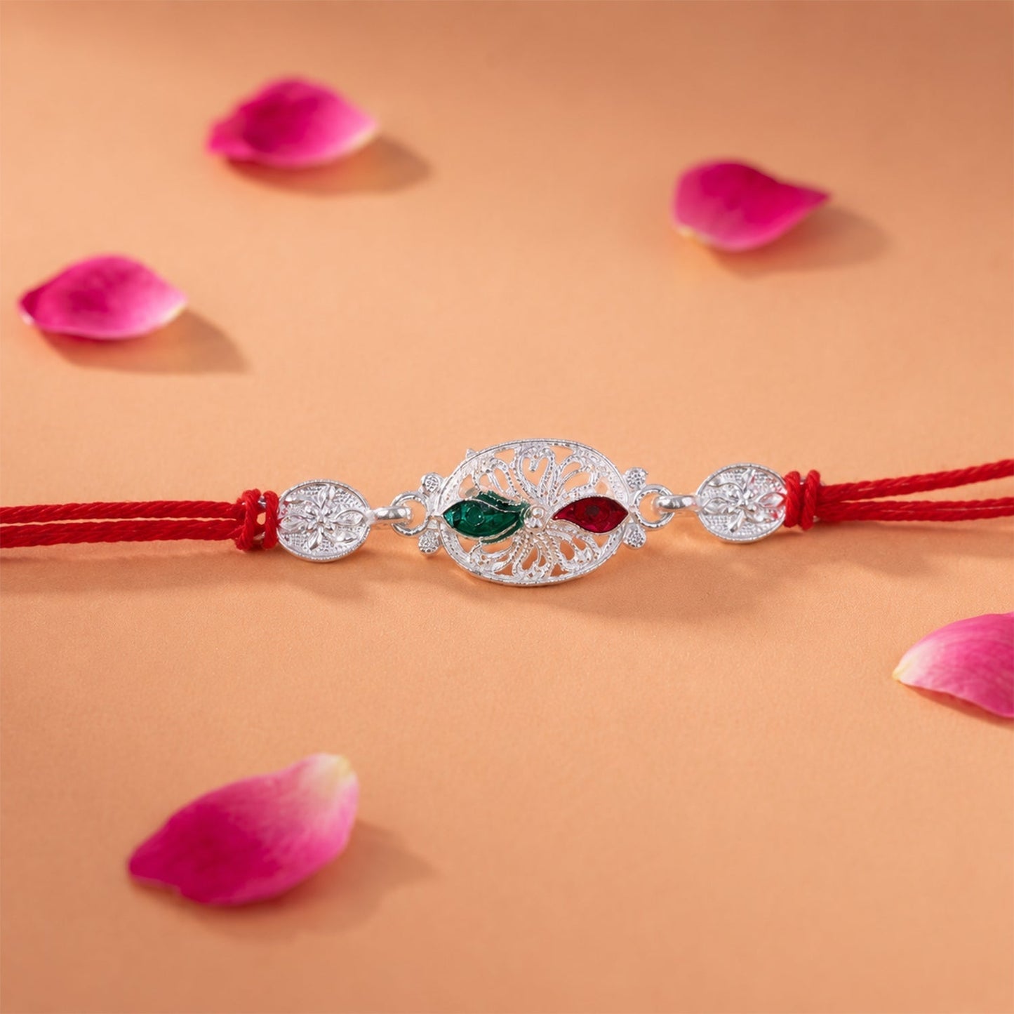Top view of silver oval Rakhi with red thread and detailed design