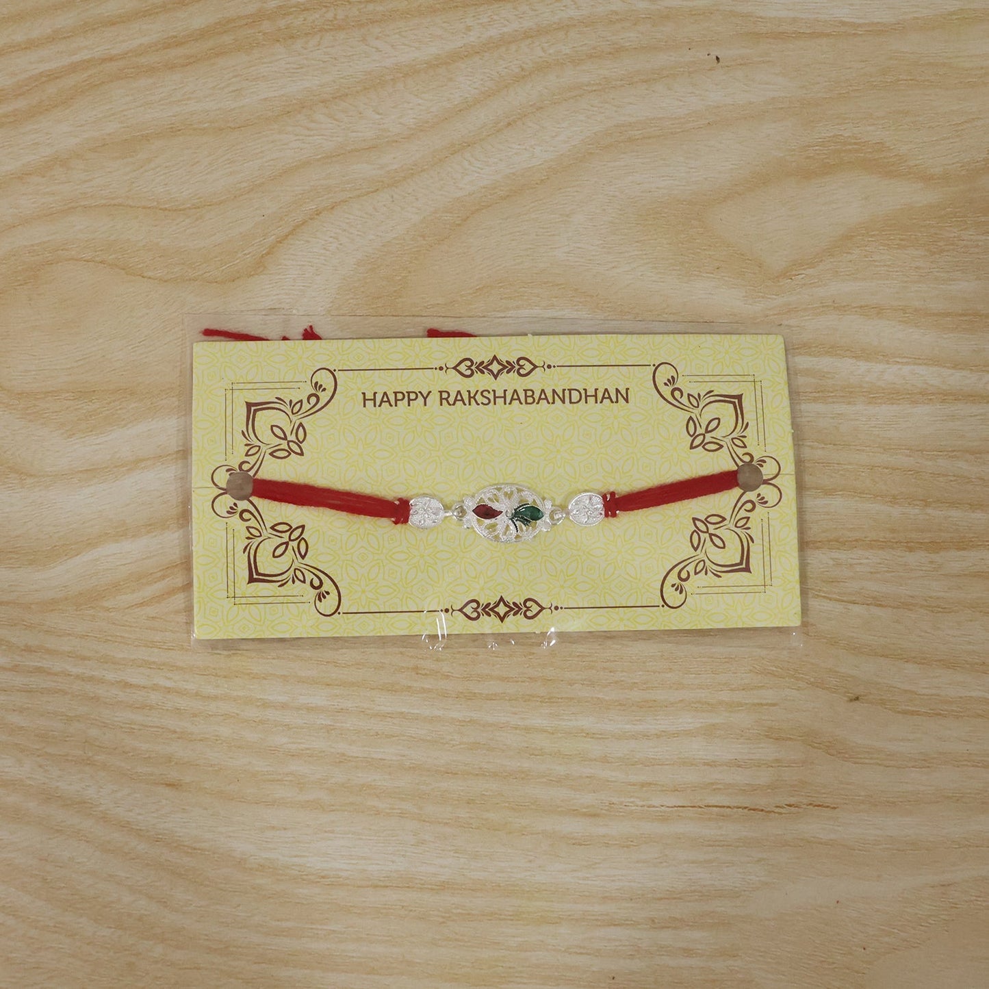 Artistic shot of silver oval Rakhi with red thread and beads