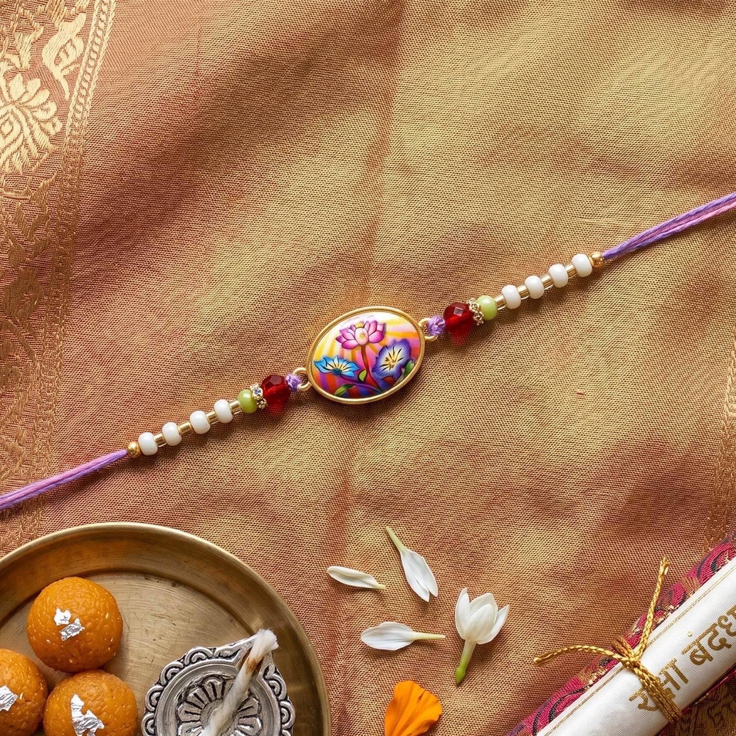 Flat display of floral designer Rakhi with purple thread