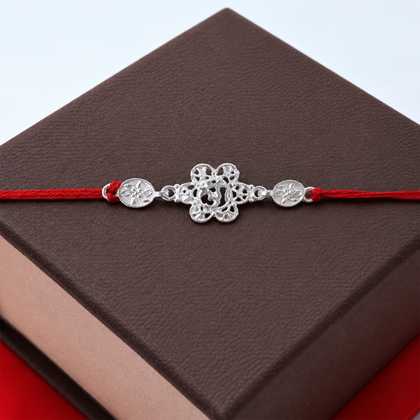 Close-up of silver floral Om Rakhi with red thread