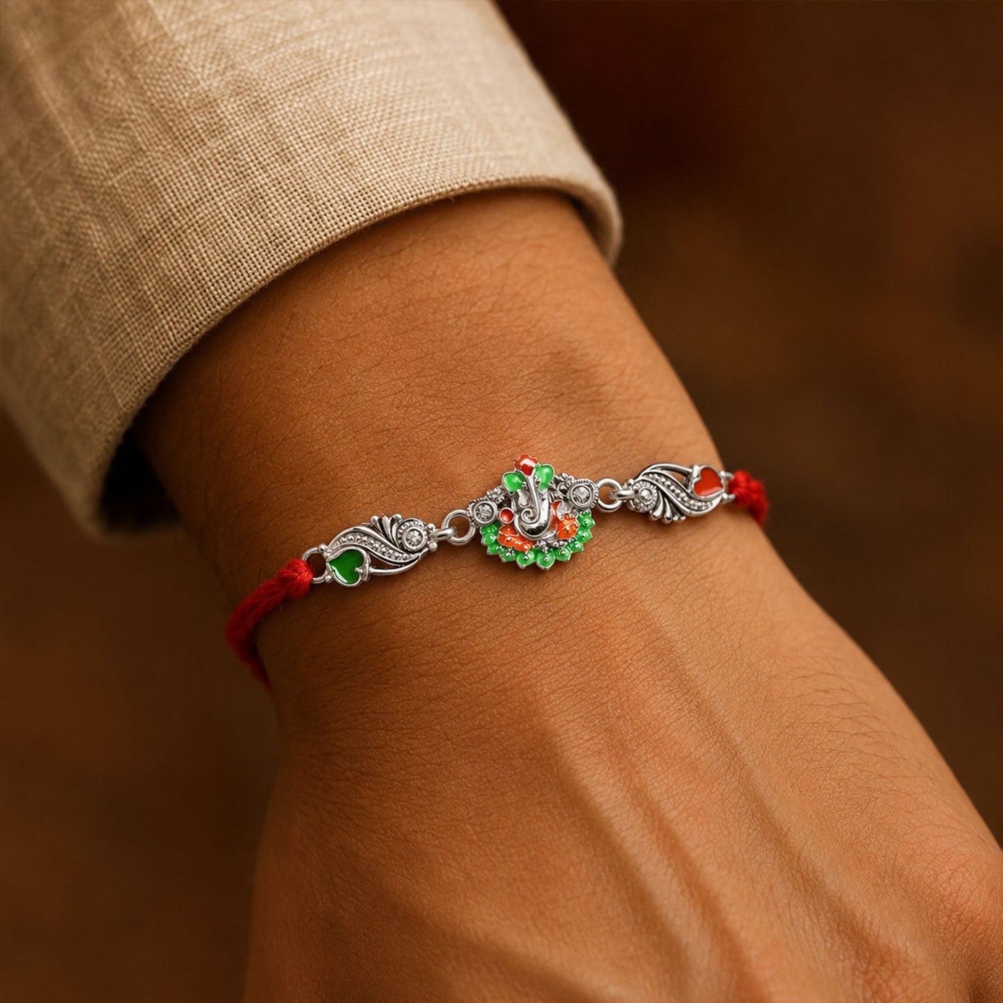 Close-up of red dori rakhi with silver Ganesh charm