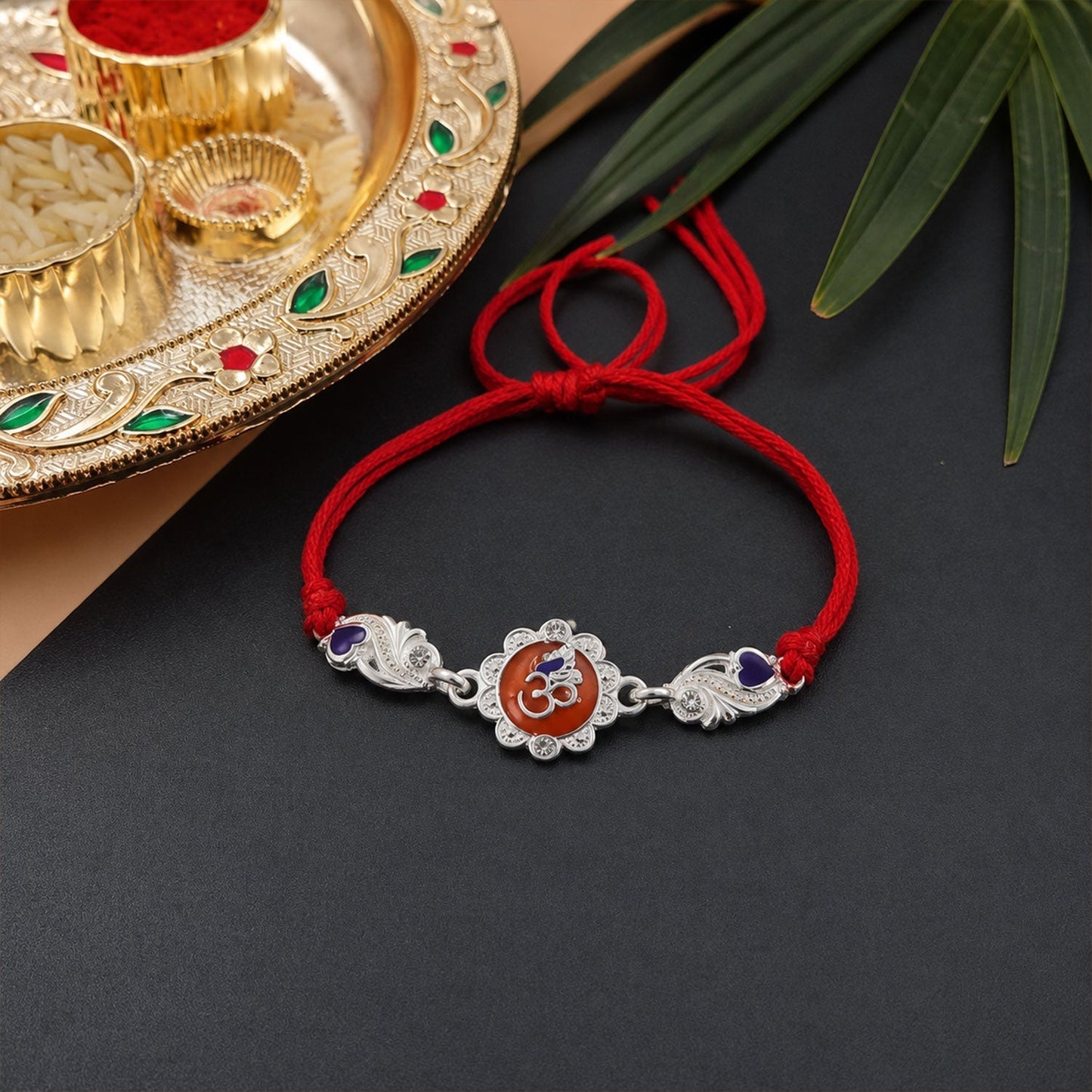Designer silver Om rakhi with detailed floral design