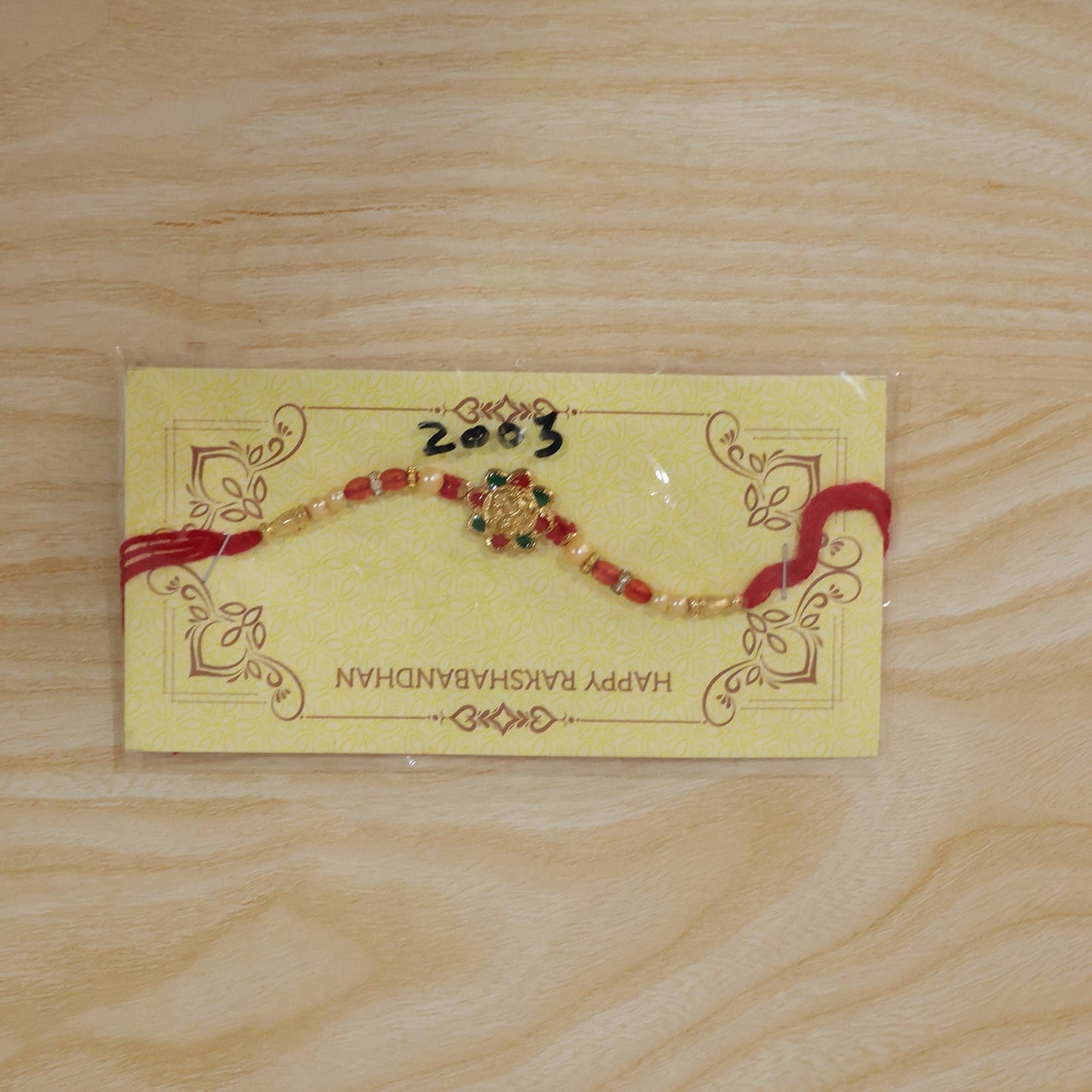 Festive rakhi with intricate meenakari work, pearls, and red beads