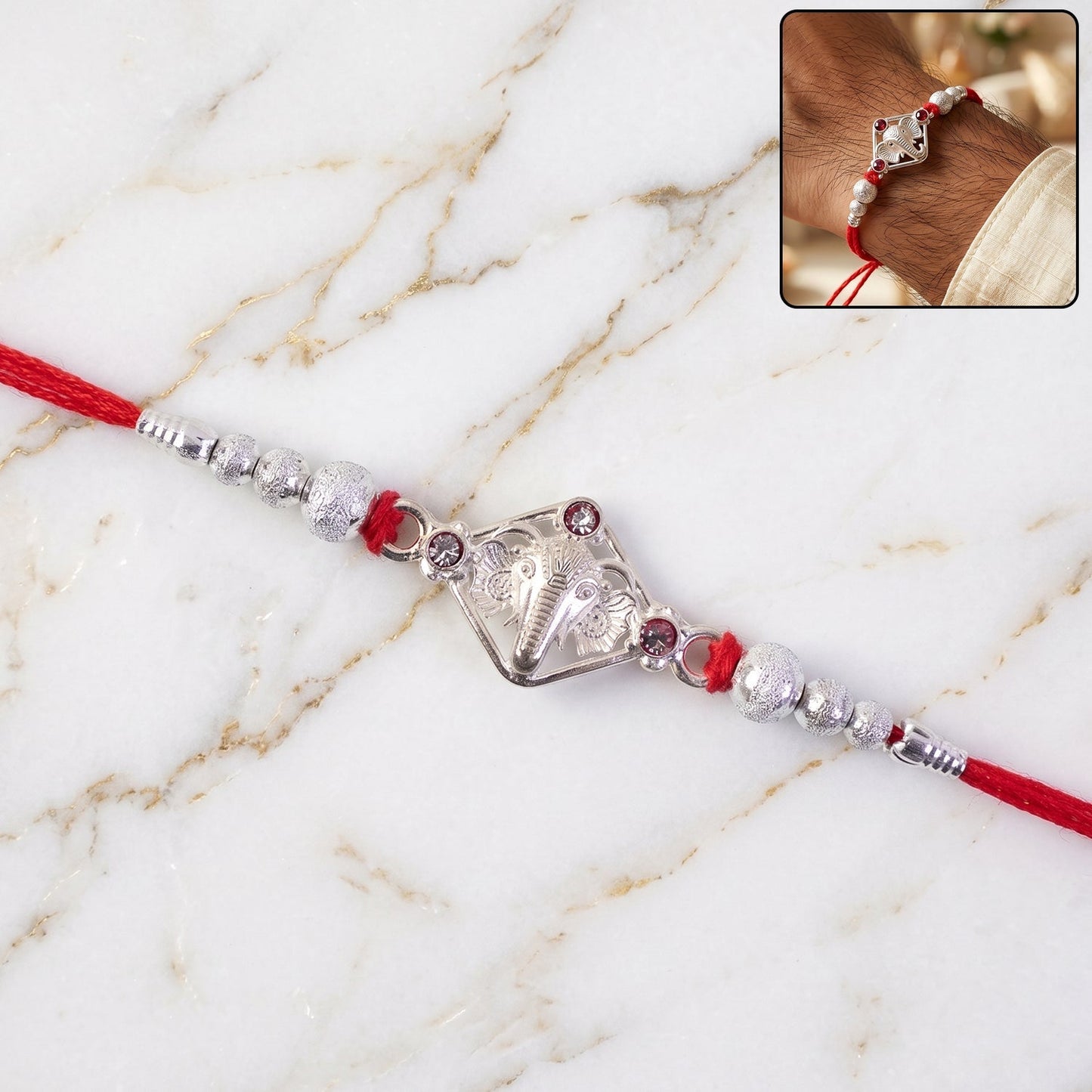 Ganesha Rakhi with intricate silver tone design and red pearl accents.