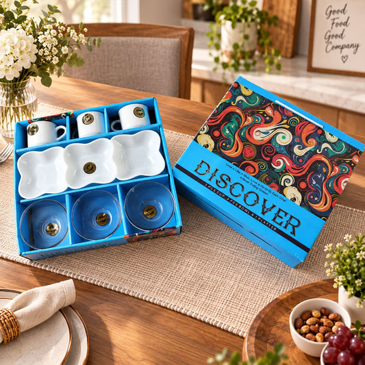 A blue gift box with a colorful abstract design on the lid sits beside the open box displaying white ceramic cups, bowls,