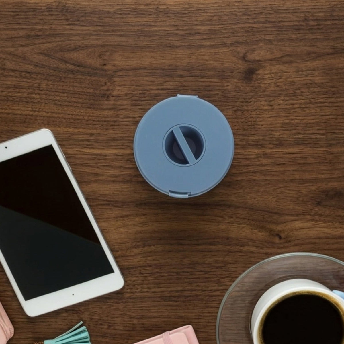 A closed blue cable winder case is centered on a wooden desk with a tablet and coffee cup.